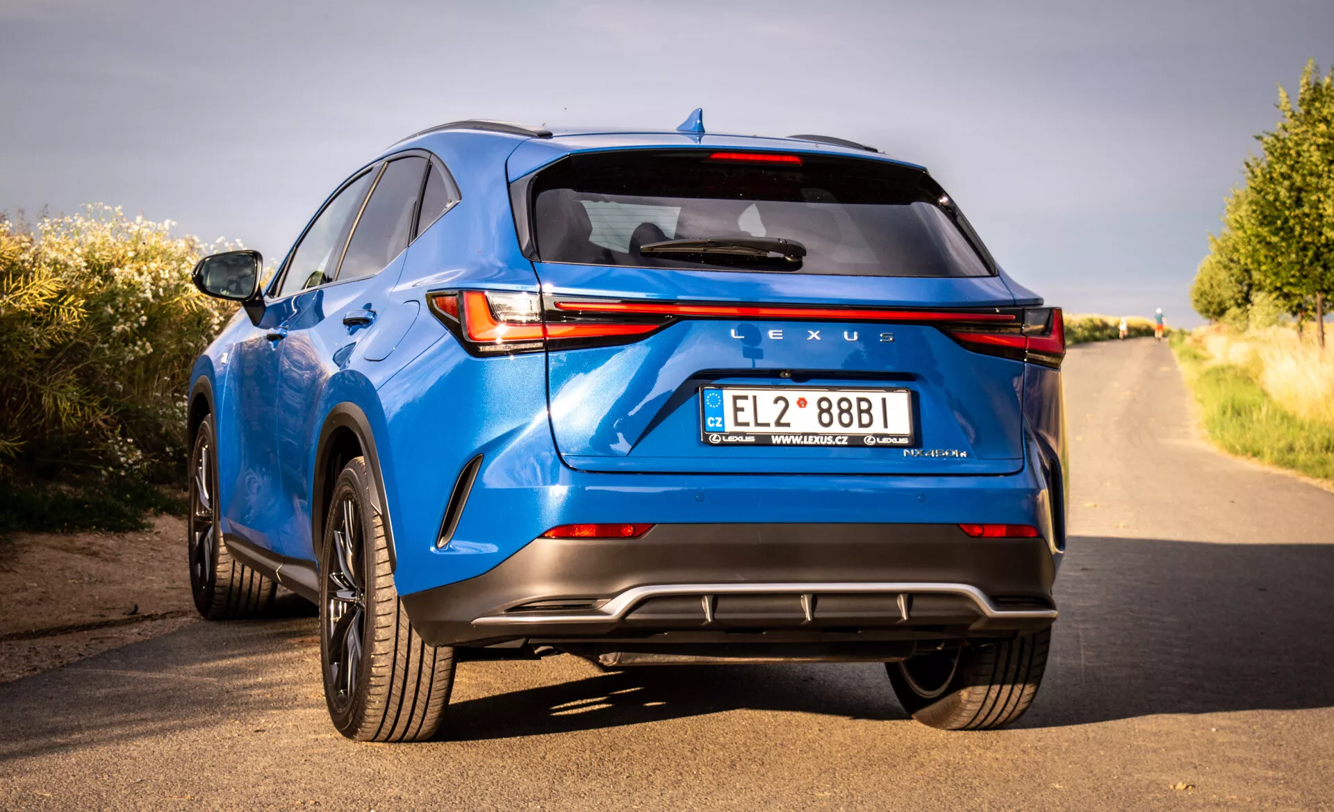 Vista trasera de un Lexus NX azul de lujo crossover SUV 2021 mostrando luces traseras LED, branding de Lexus, paragolpes trasero deportivo con difusor, tubos de escape dobles y otras características tecnológicas y de diseño desde una perspectiva de tres cuartos y bajo ángulo