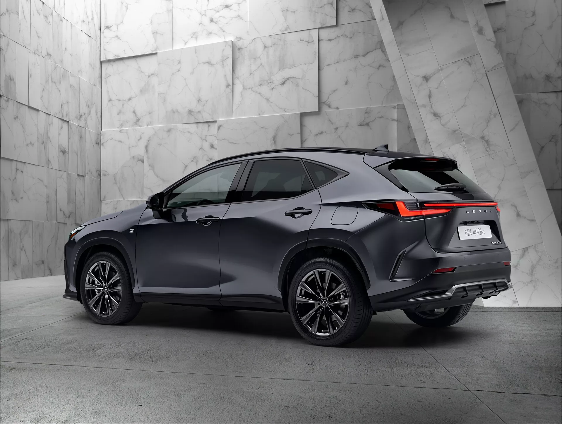 Vista trasera de tres cuartos de un moderno Lexus NX 2021 SUV en un entorno de sala de exposición. Se muestra claramente el lado derecho y trasero del vehículo, destacando las luces traseras con diseño angular LED, pintura oscura y brillante, ruedas de diseño multi-radio y la línea del techo con posibles rieles. El fondo texturizado y neutral contrasta bien con el diseño sofisticado del SUV.
