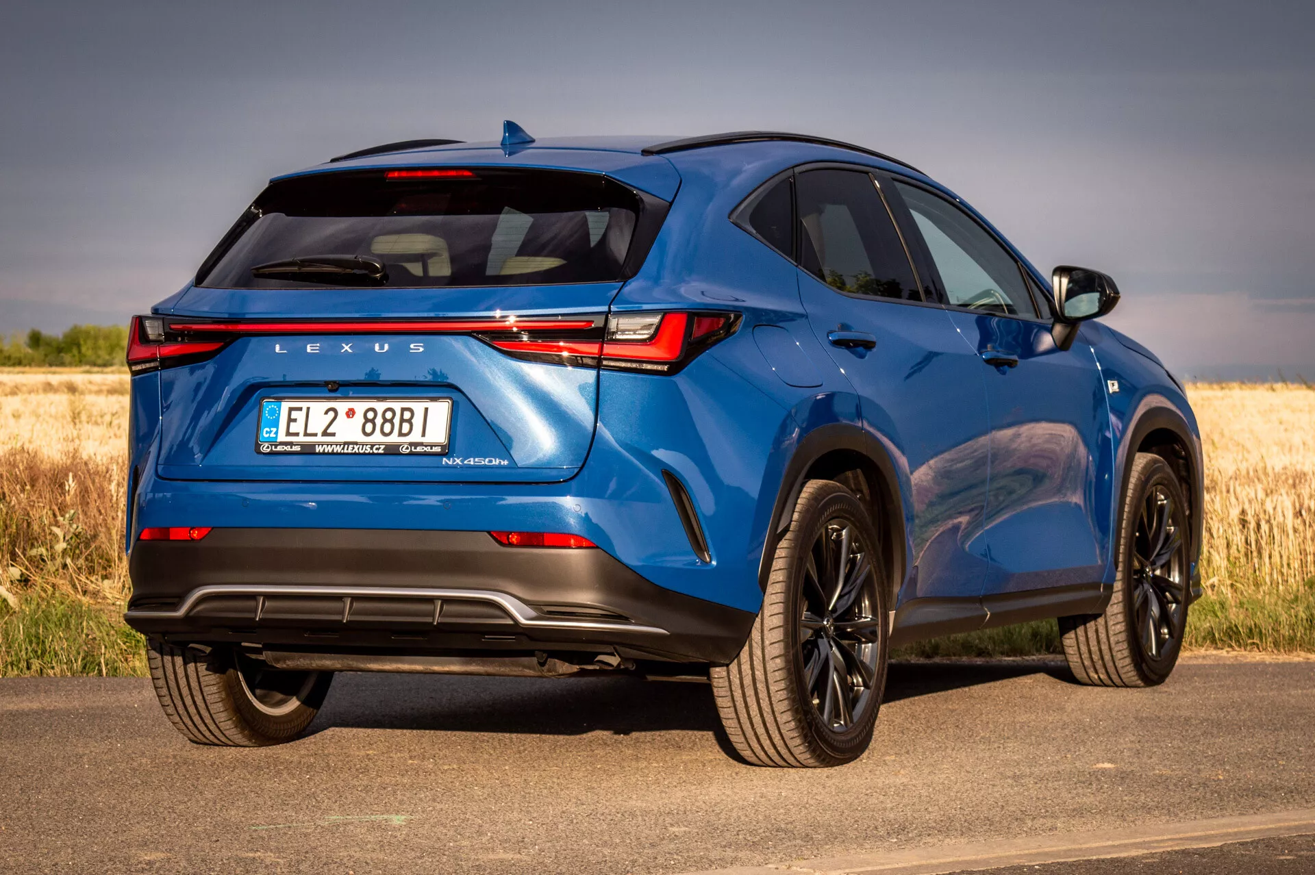 SUV azul Lexus NX 2021 en vista trasera de tres cuartos que muestra elementos de diseño y características tecnológicas en un día soleado con fondo natural