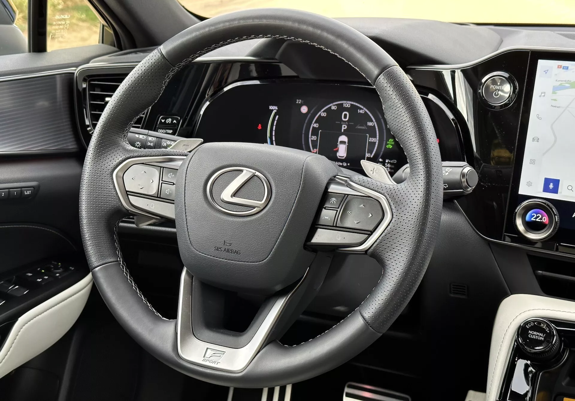 Vista interior de un Lexus NX 2021 con enfoque en el volante y el tablero, mostrando botones multifunción, un cuadro de instrumentos digital, una pantalla táctil de infotenimiento, acentos de cuero, selector de modo de conducción, ventilaciones de aire y costura detallada.