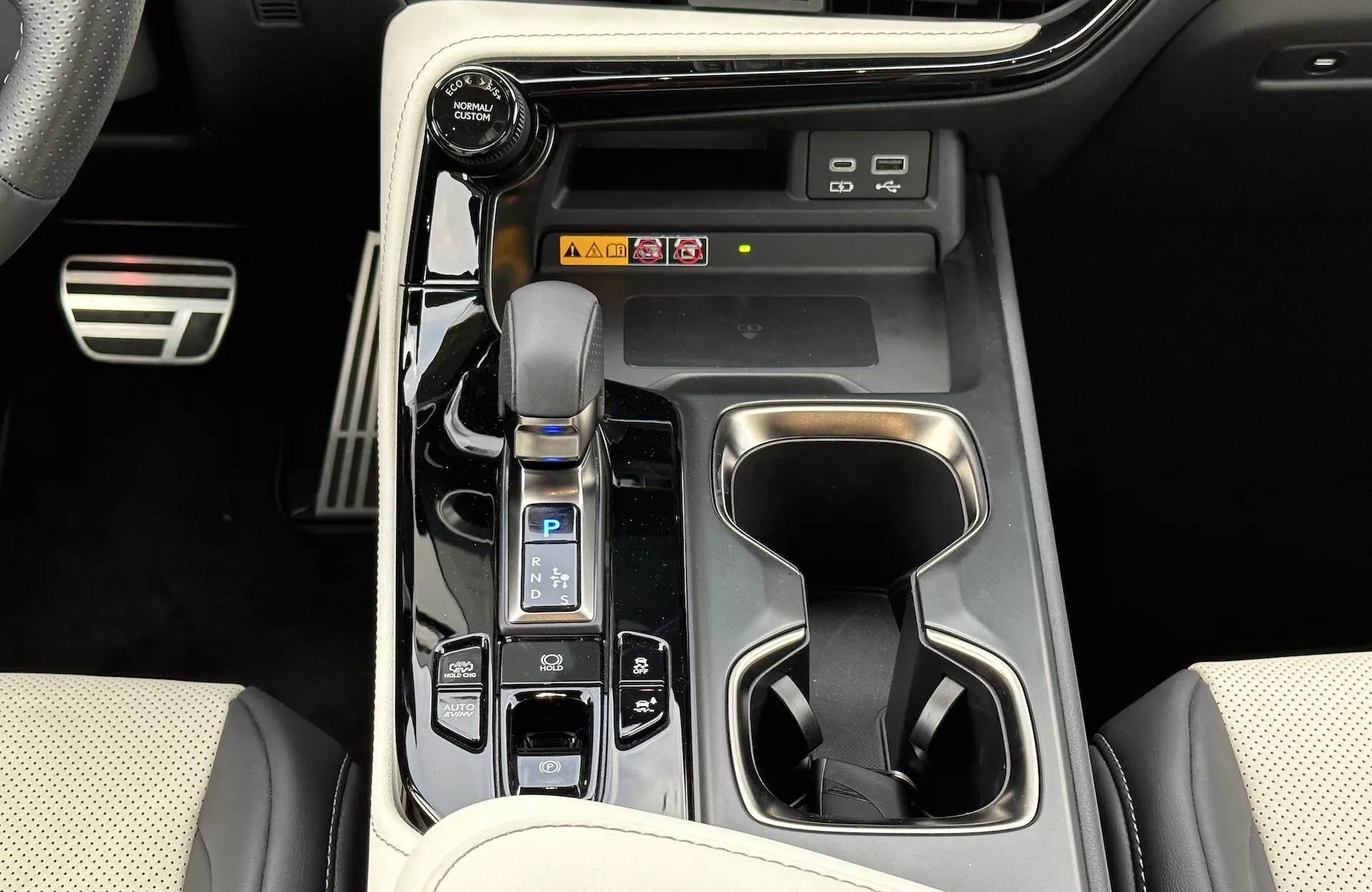Vista del centro de control del Lexus NX 2021 mostrando palanca de cambios automática con funda de cuero, selector de modo de conducción, portavasos, botones de control del vehículo, posibles accesos directos a la información y entretenimiento, y elementos de diseño interior de lujo