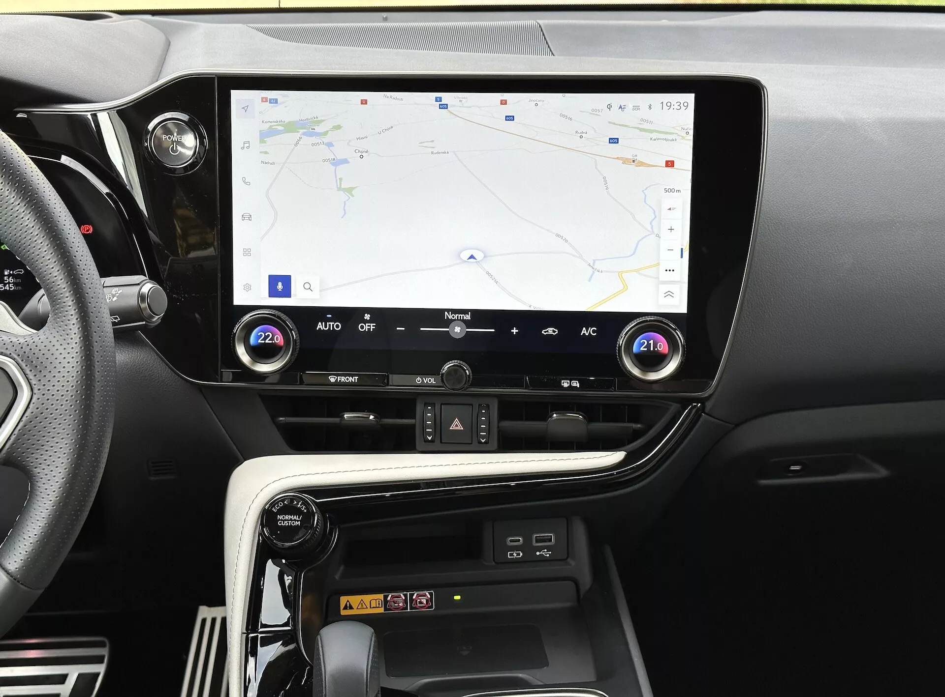 Consola central del Lexus NX 2021 con pantalla táctil que muestra la navegación GPS, botones y diales de control climático, y compartimento de carga para smartphones