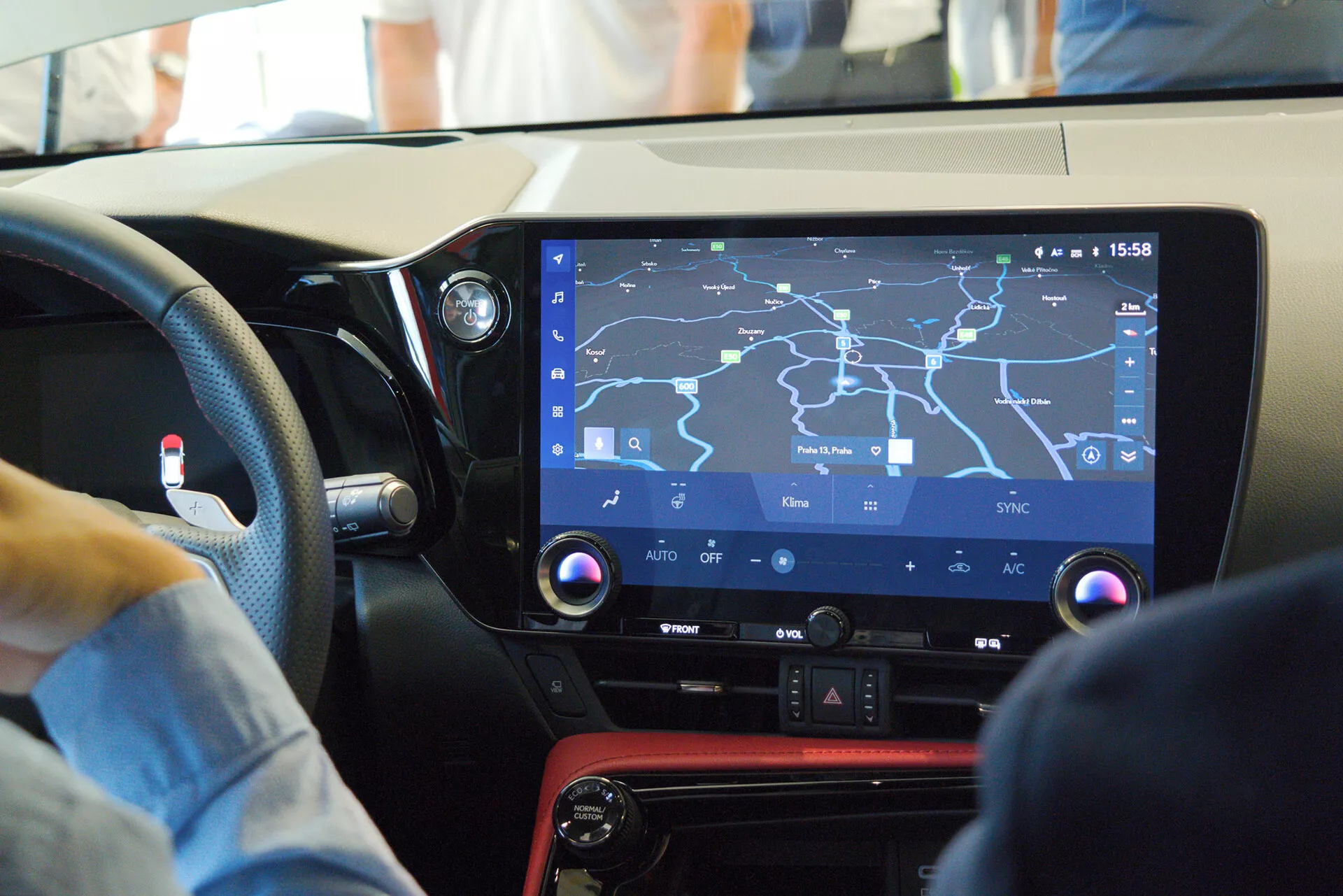 Vista interior de un coche moderno enfocándose en la consola central y el sistema de infoentretenimiento desde la perspectiva del pasajero, mostrando una gran pantalla táctil con un mapa de navegación, controles físicos para la climatización, un panel negro brillante con un acento rojo y sugiriendo un diseño amigable para el conductor en un entorno bullicioso.
