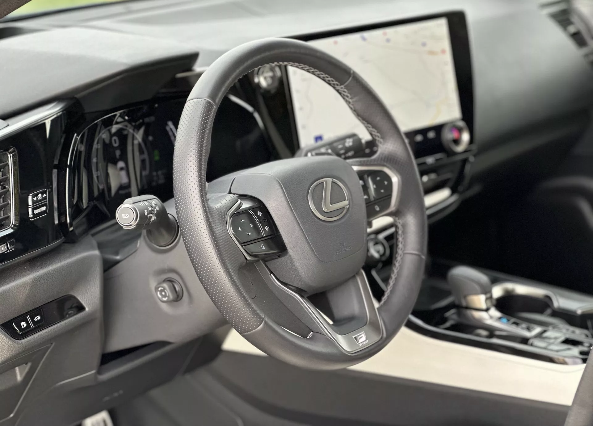 Vista interior del Lexus NX 2021 centrada en el volante forrado en cuero con controles montados y el tablero digital detrás de él, destacando la gran pantalla táctil del sistema de infoentretenimiento y sutiles pistas de lujo en los materiales de alta calidad