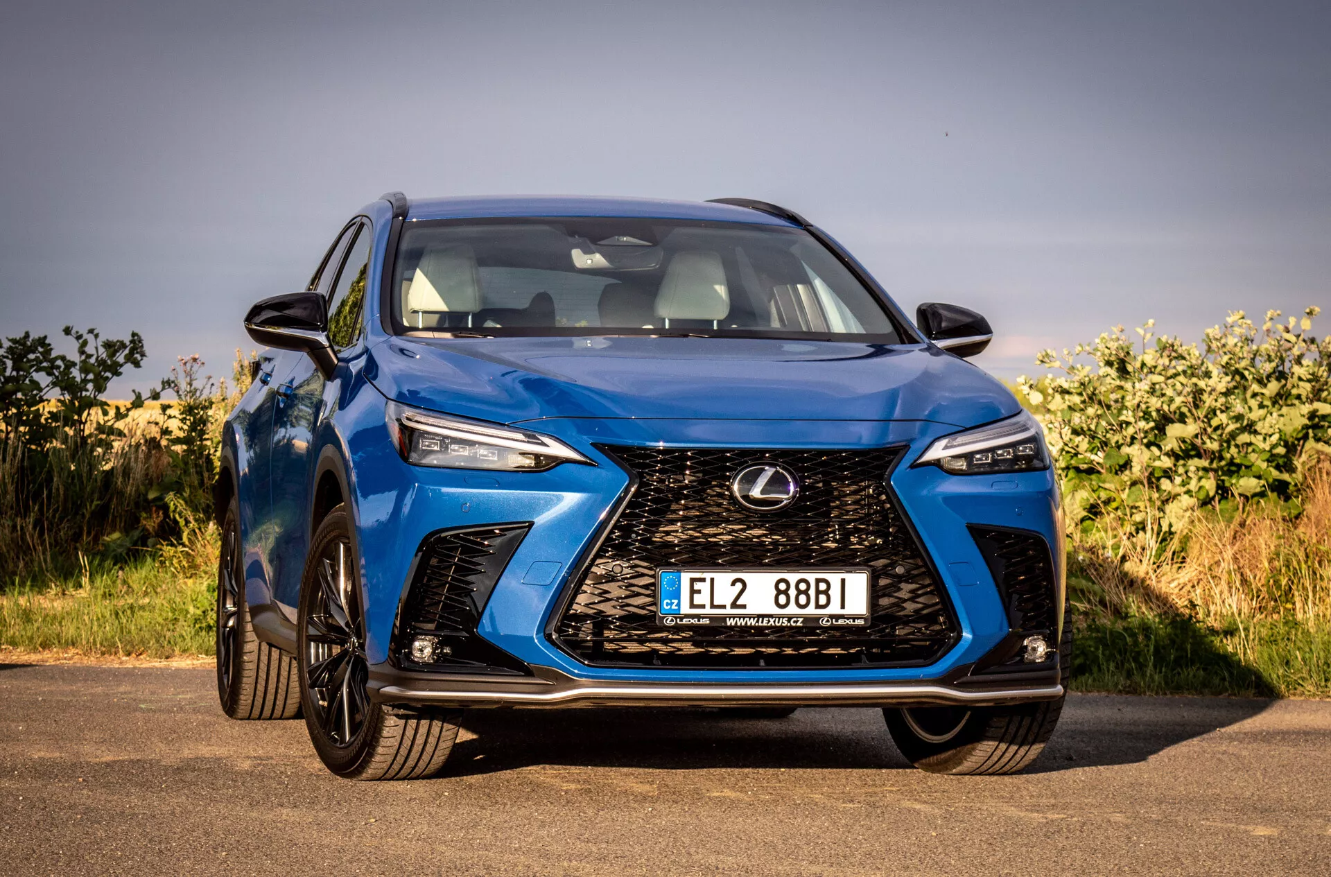 Vista frontal de un Lexus NX 2021 SUV azul destacando su parrilla espigada intrincada, faros LED angulares, acabado brillante y diseño aerodinámico, estacionado al aire libre bajo cielos despejados
