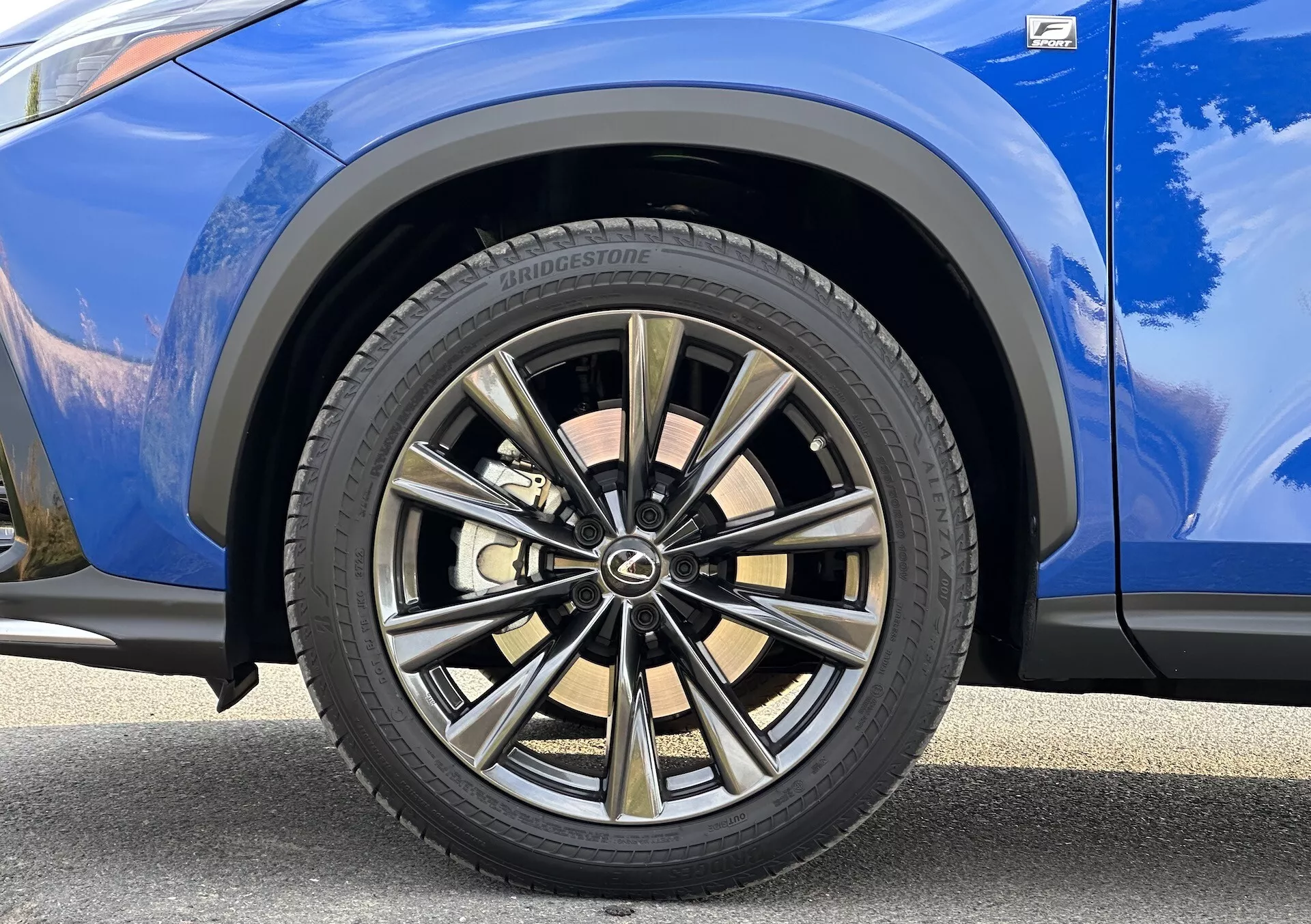 Vista detallada de la rueda delantera del lado del pasajero de Lexus NX 2021 con diseño de múltiples radios en acabado bicolor y neumático Bridgestone, con carrocería azul vibrante