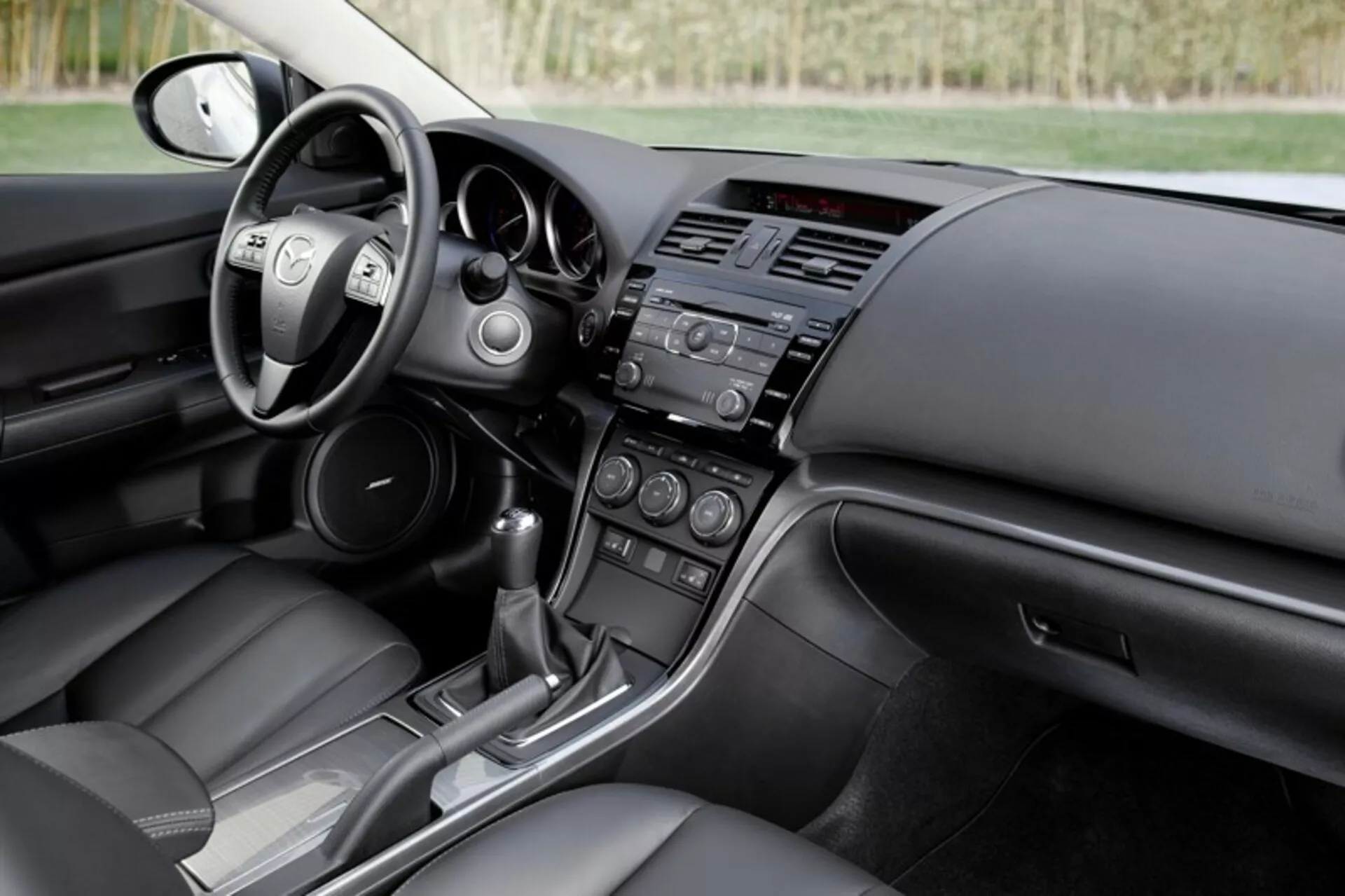 Interior del sedán Mazda 6 2008 mostrando la cabina del conductor y la vista del tablero del pasajero con controles en el volante, sistemas de infoentretenimiento y control climático, y consola de transmisión automática, destacando diseño moderno y características tecnológicas del coche.