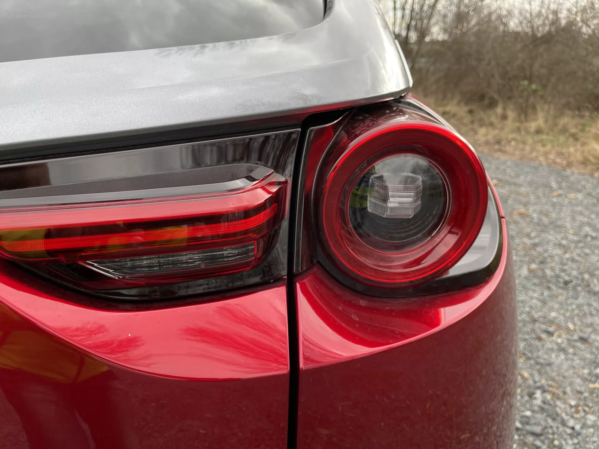 Vista detallada de la esquina trasera de un Mazda MX-30 2020 mostrando el diseño detallado de la luz trasera, pintura roja brillante y reflejo en su carrocería, destacando la tecnología de iluminación y diseño de vehículos modernos.