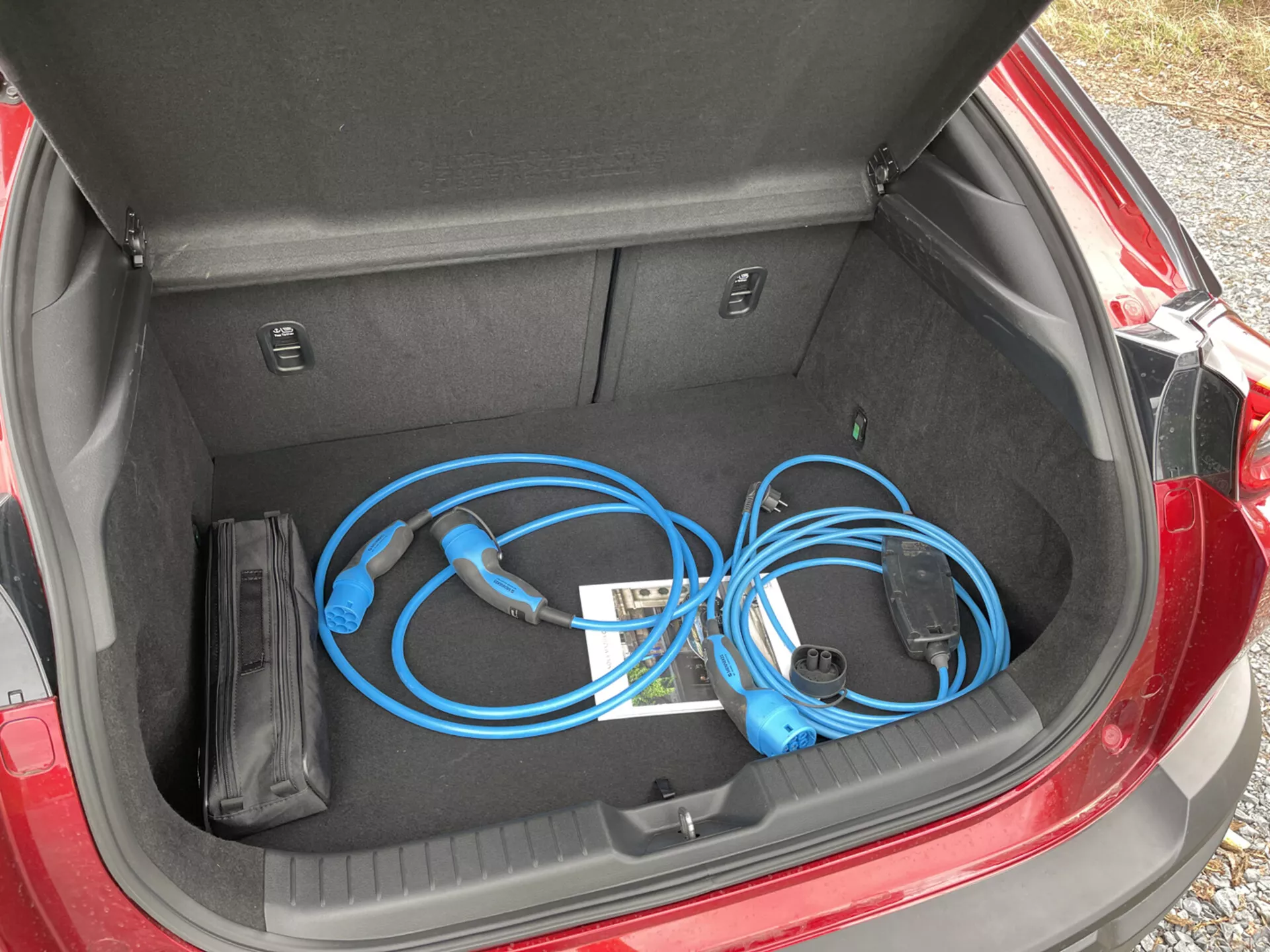Maletero abierto del Mazda MX-30 2020 mostrando un cable de carga portátil para vehículos eléctricos con una vista cercana y desde arriba a la izquierda, mostrando el espacio de almacenamiento limpio y plano junto con compartimientos internos.