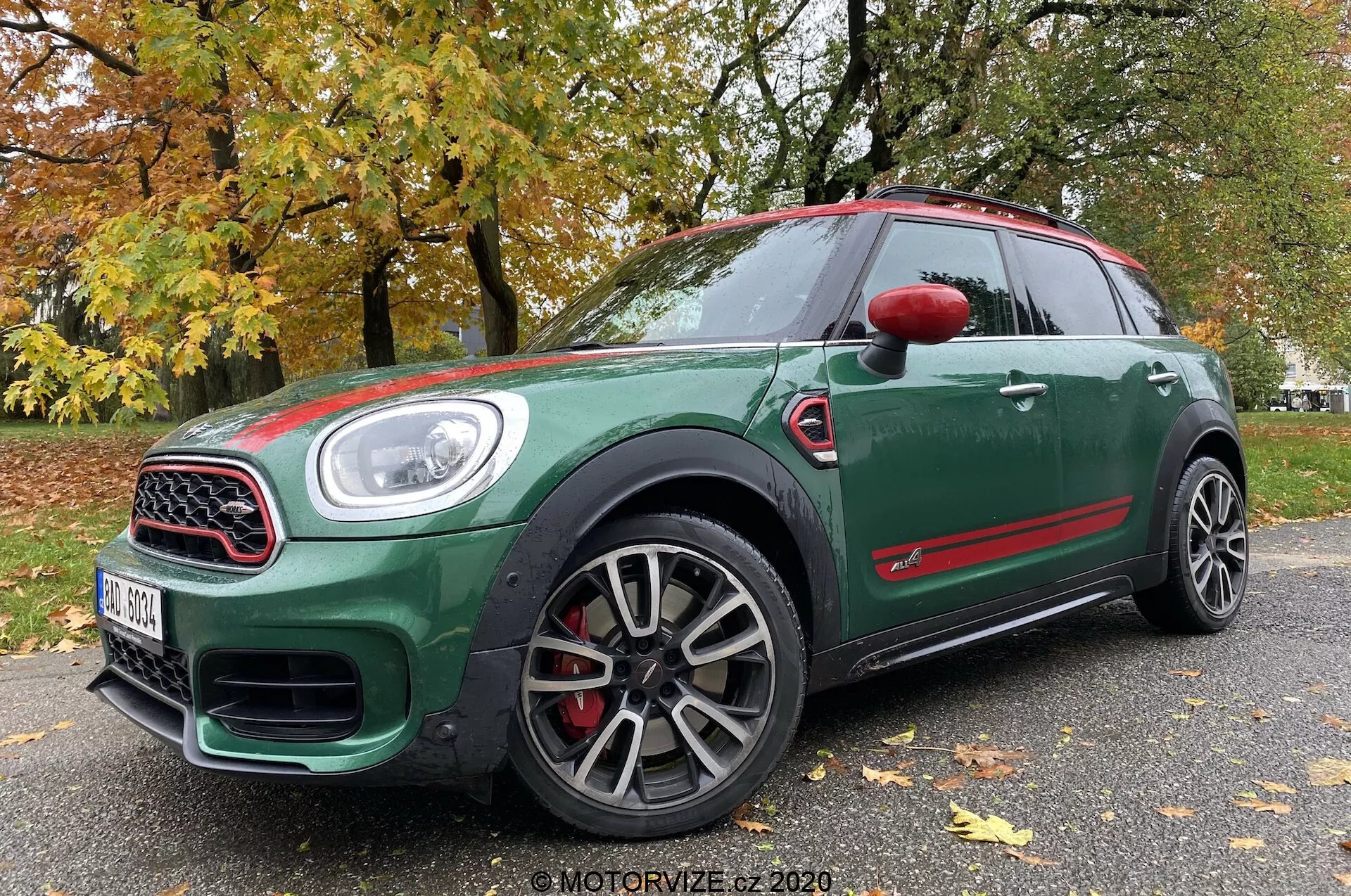 Vista frontal en tres cuartos de bajo ángulo de un Mini Countryman John Cooper Works 2020, que muestra su exterior verde oscuro con detalles rojos, ruedas deportivas de múltiples radios, parrilla con marco de cromo, grandes entradas de aire, faros LED y pinzas de freno rojas.
