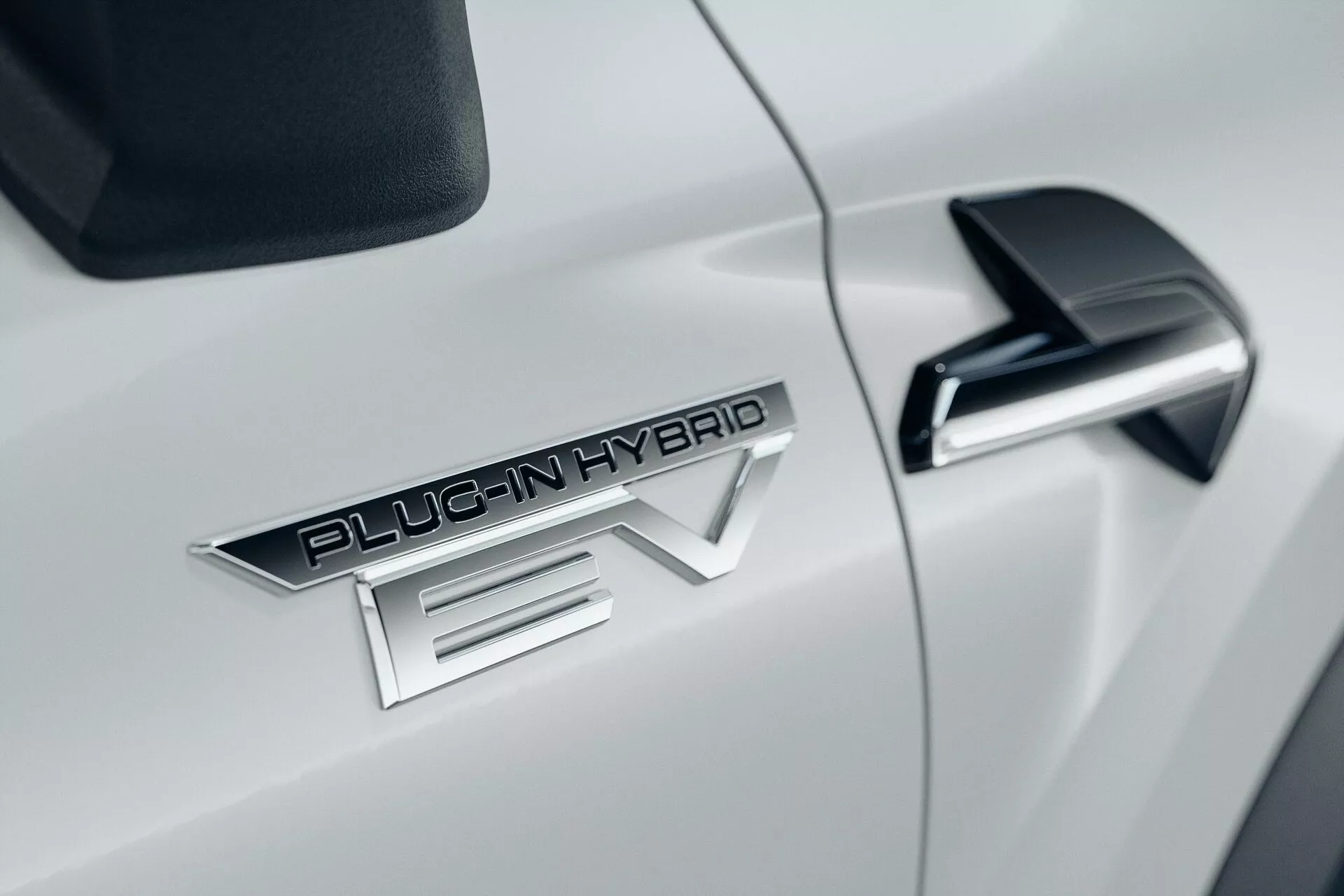Primer plano del lado del coche blanco Mitsubishi ASX 2023 de segunda generación, con el distintivo prominente 'PLUG-IN HYBRID EV', elegante espejo lateral negro con señal de giro integrada y carrocería aerodinámica blanca brillante.