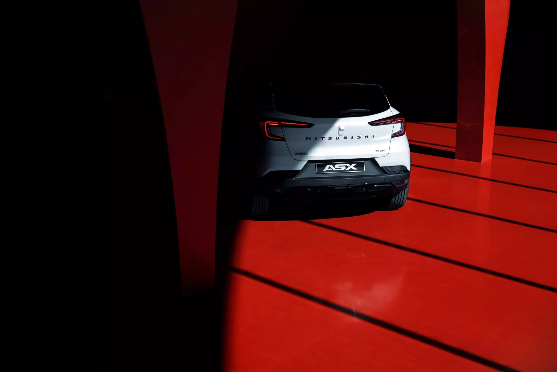 Toma en ángulo bajo del extremo trasero del SUV compacto Mitsubishi ASX 2023 con luces traseras esculpidas, insignia de cromo y parabrisas trasero, capturada a la luz del día de alto contraste en un suelo rojo vivo.