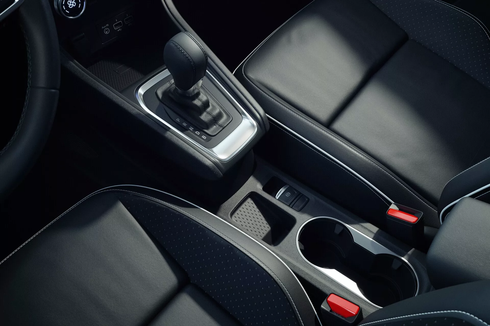 Imagen interior del centro de la consola del Mitsubishi ASX 2023 de segunda generación tomada desde un ángulo cenital centrándose en detalles como la palanca de cambios de cuero, acentos en cromo alrededor del área de cambios, compartimiento de almacenamiento con bandeja extraíble, dos portavasos con bordes cromados, asientos de cuero negro con costuras visibles, botón de freno de estacionamiento electrónico y reposabrazos central parcialmente visible, mostrando materiales de alta calidad y diseño moderno.