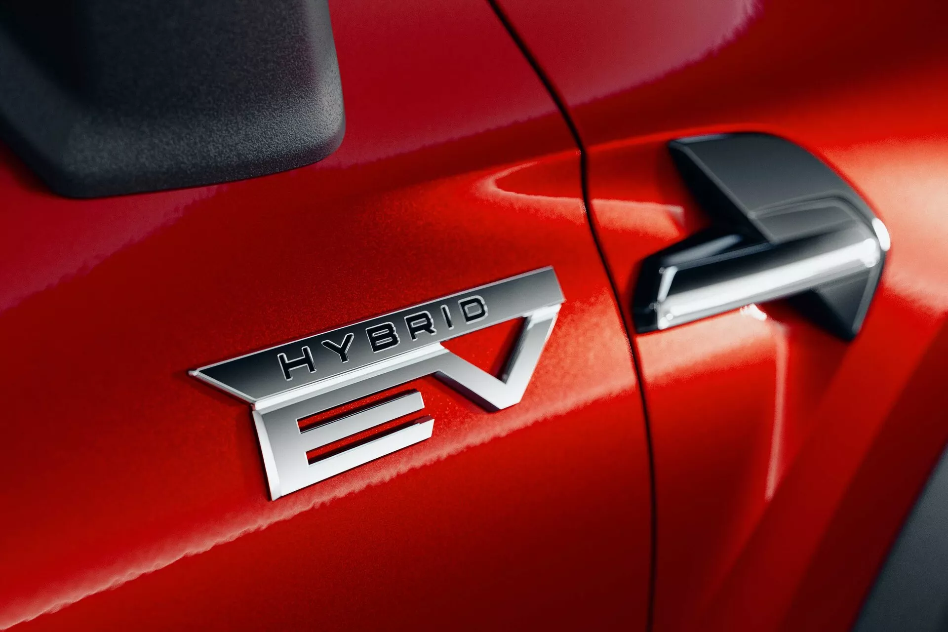 Detalle en primer plano del Mitsubishi ASX 2023 (2ª generación) en rojo, destacando la insignia 'HYBRID EV' que indica la tecnología de vehículo eléctrico híbrido. La insignia 'HYBRID EV' está centrada, resaltando el acabado metálico y las letras precisas. El 'EV' presenta un diseño distintivo con una flecha que atraviesa la 'V'. Parte del espejo retrovisor lateral se ve en la esquina superior derecha, sugiriendo características tecnológicas adicionales. El acabado brillante de la pintura y la costura firme entre la puerta del pasajero delantero y el guardabarros delantero sugieren una calidad de construcción superior.