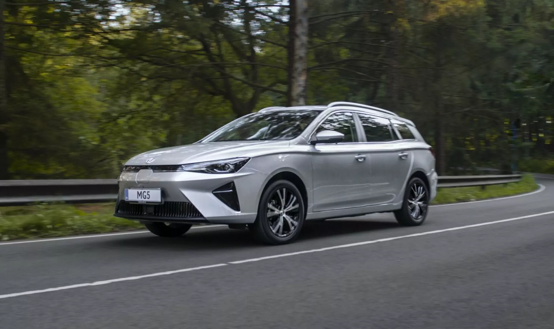Mitsubishi Outlander Plug-In Hybrid 2018 en movimiento en una carretera rodeada de árboles, mostrando su diseño elegante y faros LED, con un fondo verde difuminado que enfatiza la velocidad y la tecnología ecológica.