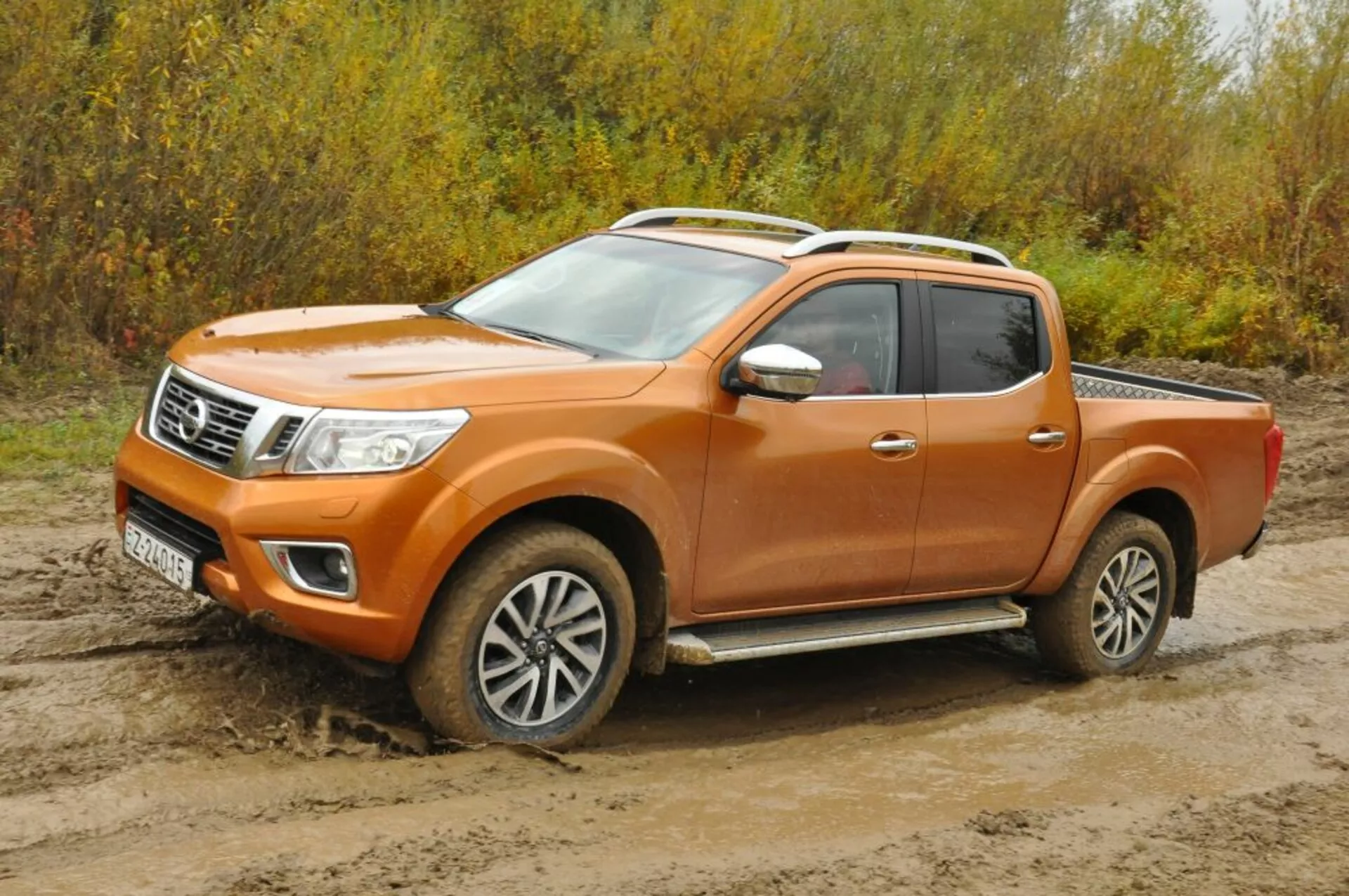Camioneta Nissan Navara naranja de 2016 en vista frontal de tres cuartos, mostrando faros, parrilla con acabados de cromo, ruedas de aleación y configuración de cabina para la tripulación en terreno accidentado