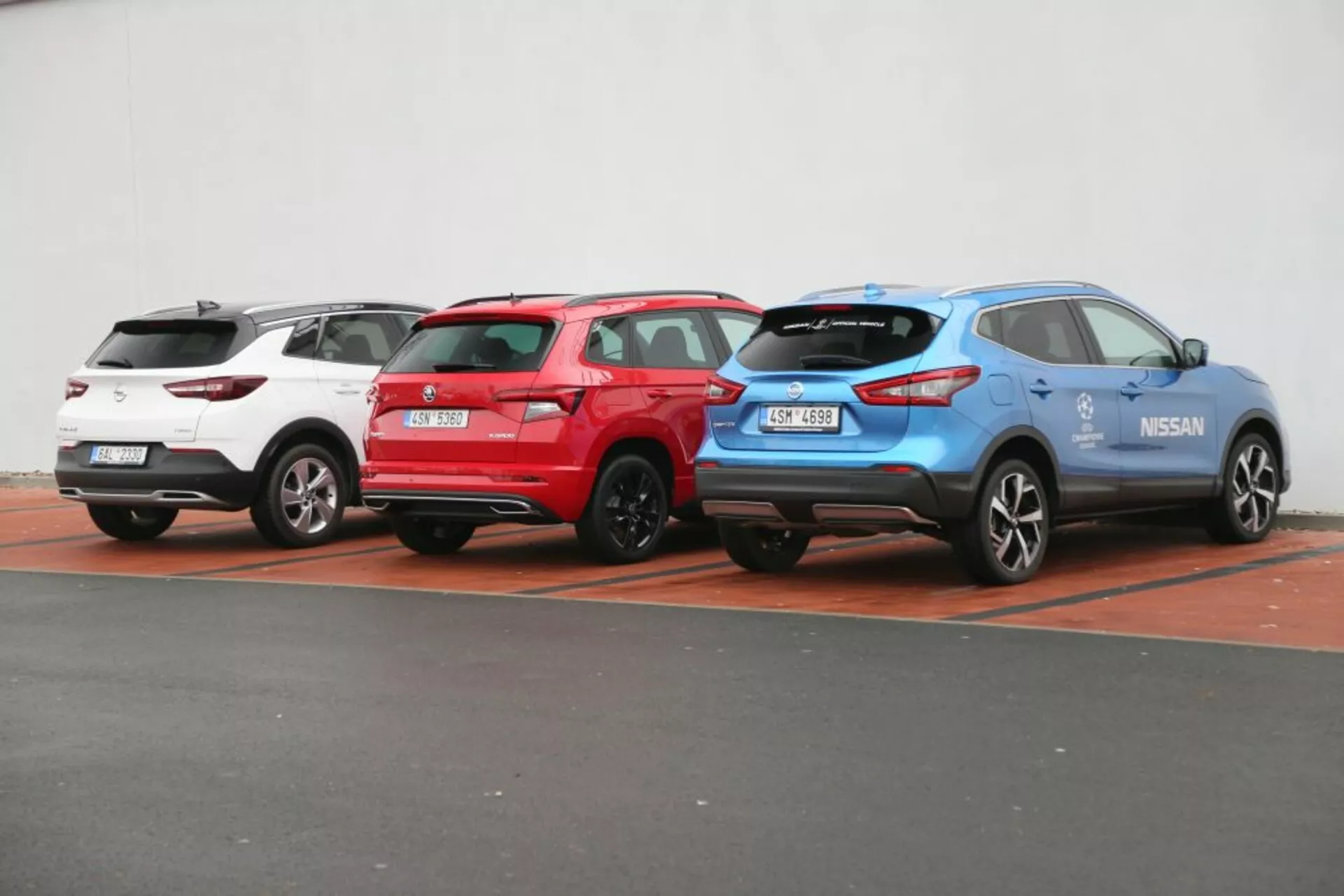 Tres SUV Nissan Qashqai 2014 en blanco, rojo y azul estacionados uno al lado del otro mostrando perfiles traseros y laterales con luces traseras visibles, limpiaparabrisas trasero y llantas de aleación deportivas contra un fondo discreto.