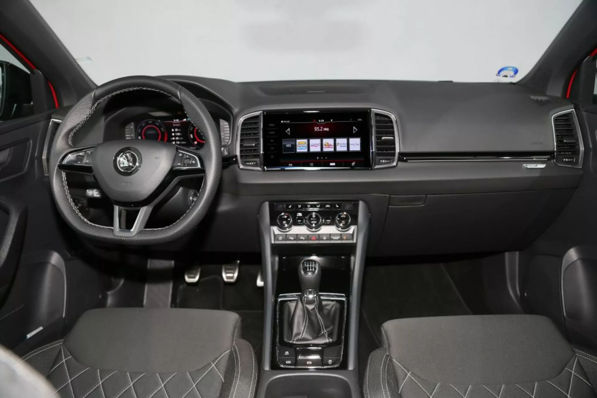 Vista frontal del interior del Nissan Qashqai 2014 mostrando el tablero, volante con controles, sistema de infoentretenimiento, palanca de cambios manual, control de clima y asientos de tela con costuras en forma de diamante.