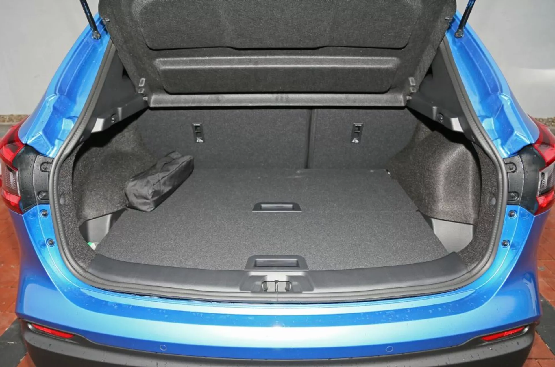 Vista detallada del maletero abierto de un Nissan Qashqai 2014, mostrando su generoso espacio de carga y características de diseño como el suelo de alfombra gris y la protección de umbral de parachoques, con un indicio del acabado exterior azul del vehículo.