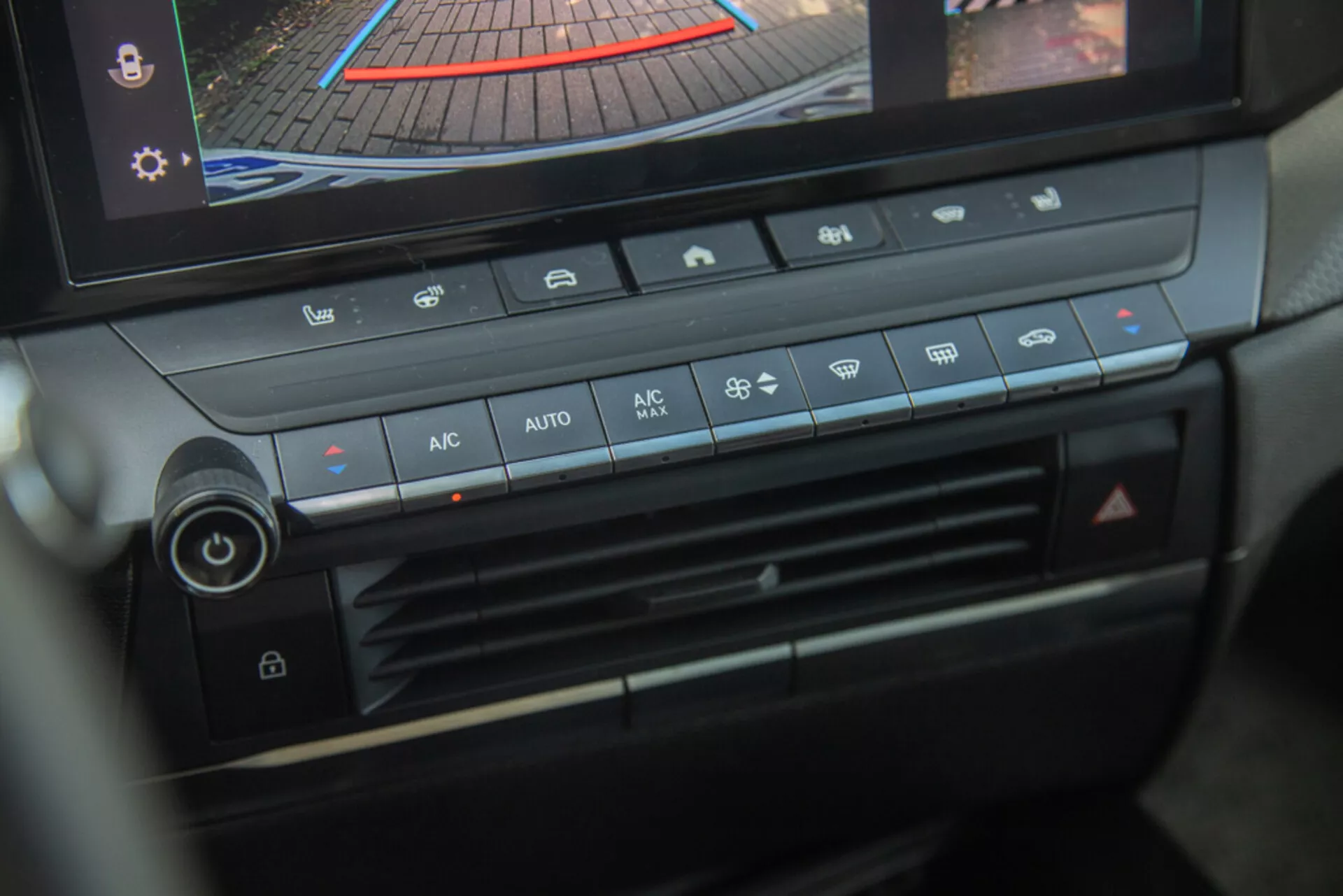 Consola central y panel de control climático del Opel Astra 2022, destacando el botón de ajuste de temperatura, velocidad del ventilador, distribución de aire y botones de control climático automático con pantalla digital mostrando cámara trasera