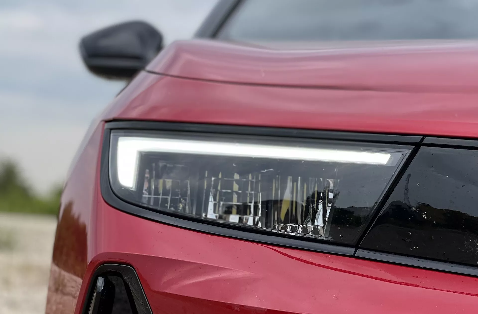 Primer plano lateral frontal de un Opel Astra rojo 2022 enfocando el diseño detallado del faro LED, mostrando la tecnología de iluminación moderna y los contornos del vehículo
