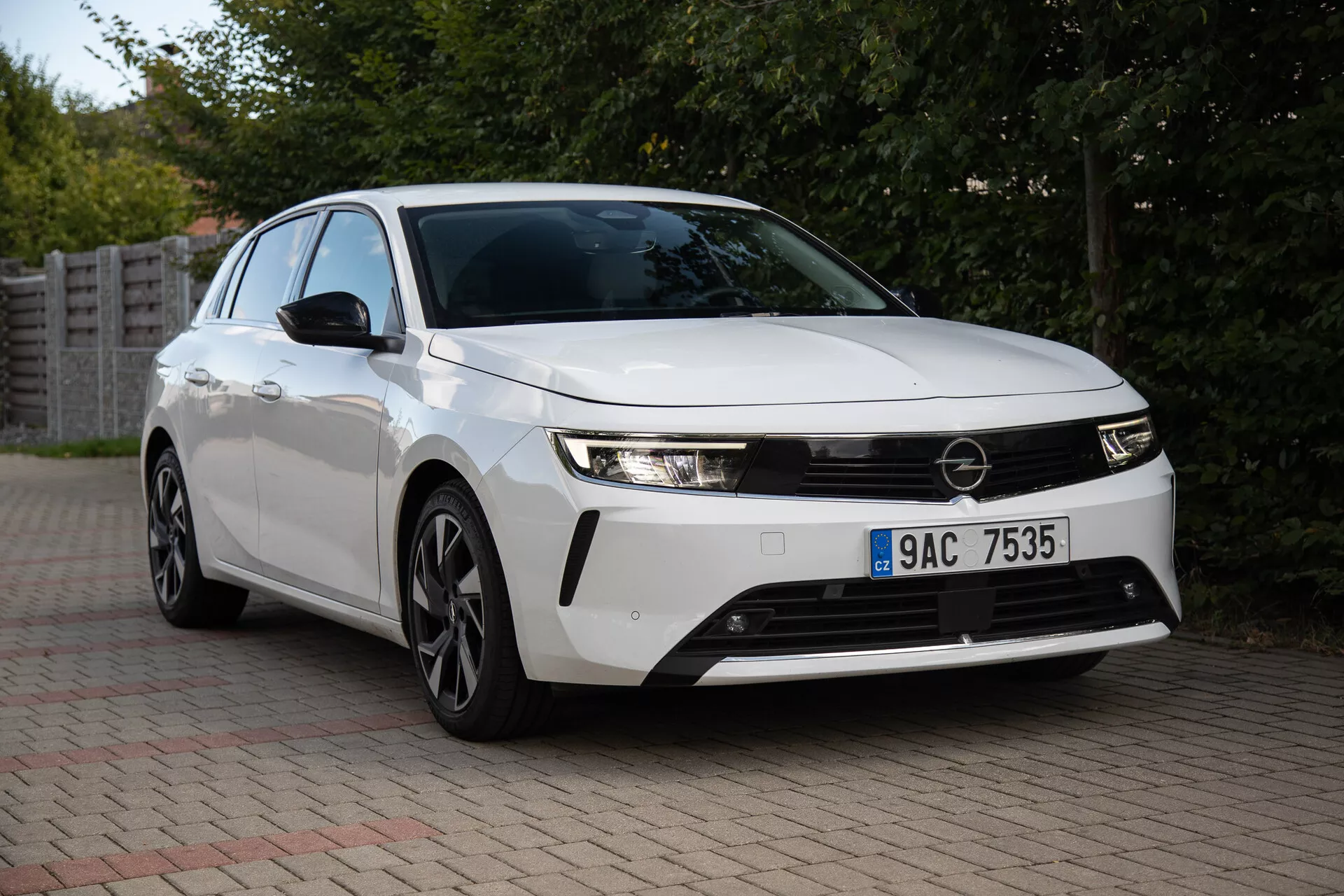 Opel Astra 2022 capturado en un entorno suburbano, mostrando sus elegantes faros, parrilla frontal prominente, diseño aerodinámico incluyendo ruedas de aleación de múltiples radios, y tecnología innovadora desde una vista frontal de tres cuartos