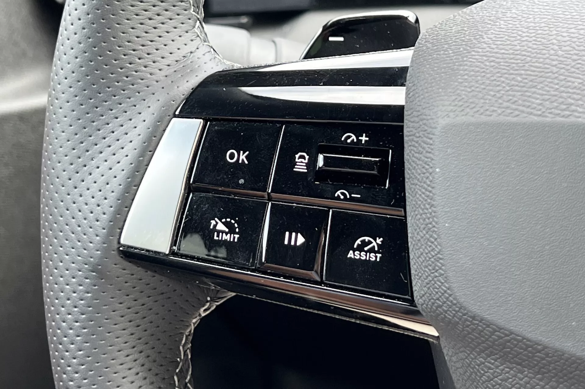Vista detallada del conjunto de botones del volante del Opel Astra 2022, destacando las características avanzadas de asistencia al conductor, incluido el control de crucero adaptativo y la asistencia de mantenimiento de carril, con enfoque en etiquetas de funcionalidad como OK, +, -, LIMIT, y ASSIST desde la perspectiva del conductor