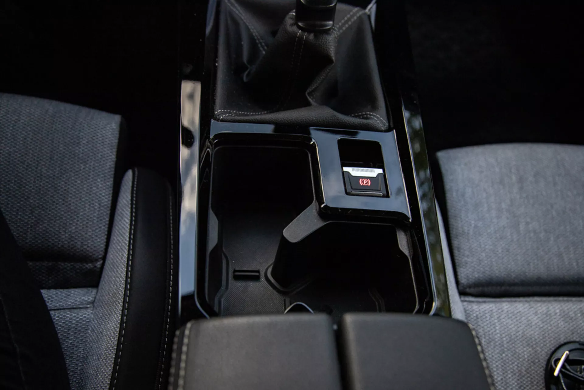 Detalle de la consola central del Opel Astra 2022 mostrando compartimento de almacenamiento abierto, tapicería de tela, palanca de cambios manual con cuero perforado, puerto USB y iluminación interior
