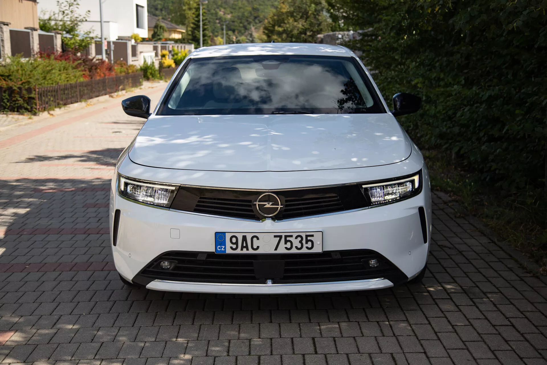 Vista frontal del Opel Astra 2022 mostrando un diseño moderno de vehículo eléctrico con faros LED, parrilla decorativa y forma aerodinámica, estacionado en la entrada de una residencia