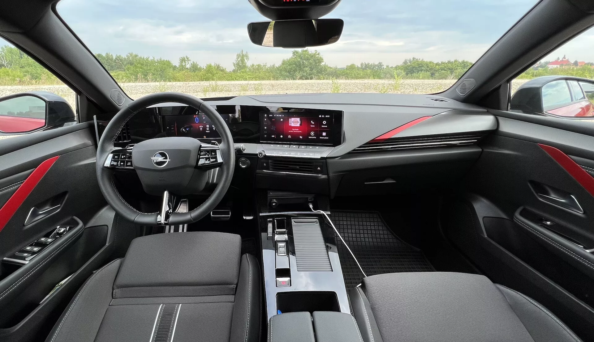 Interior del Opel Astra 2022 que muestra volante multifunción de tres radios, panel de instrumentos digital, sistema de infoentretenimiento táctil, controles elegantes de climatización, acabados en cuero bicolores con costuras rojas y diseño moderno del habitáculo desde la perspectiva del conductor