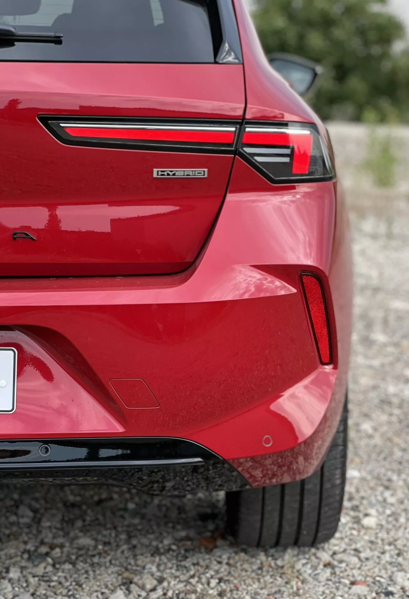Toma detallada del cuarto trasero del Opel Astra 2022 en rojo, mostrando luces traseras LED, posible spoiler integrado en el maletero, emblema '-tron' que sugiere modelo eléctrico o híbrido, parachoques con sensores de estacionamiento, llanta deportiva y acabado metálico brillante