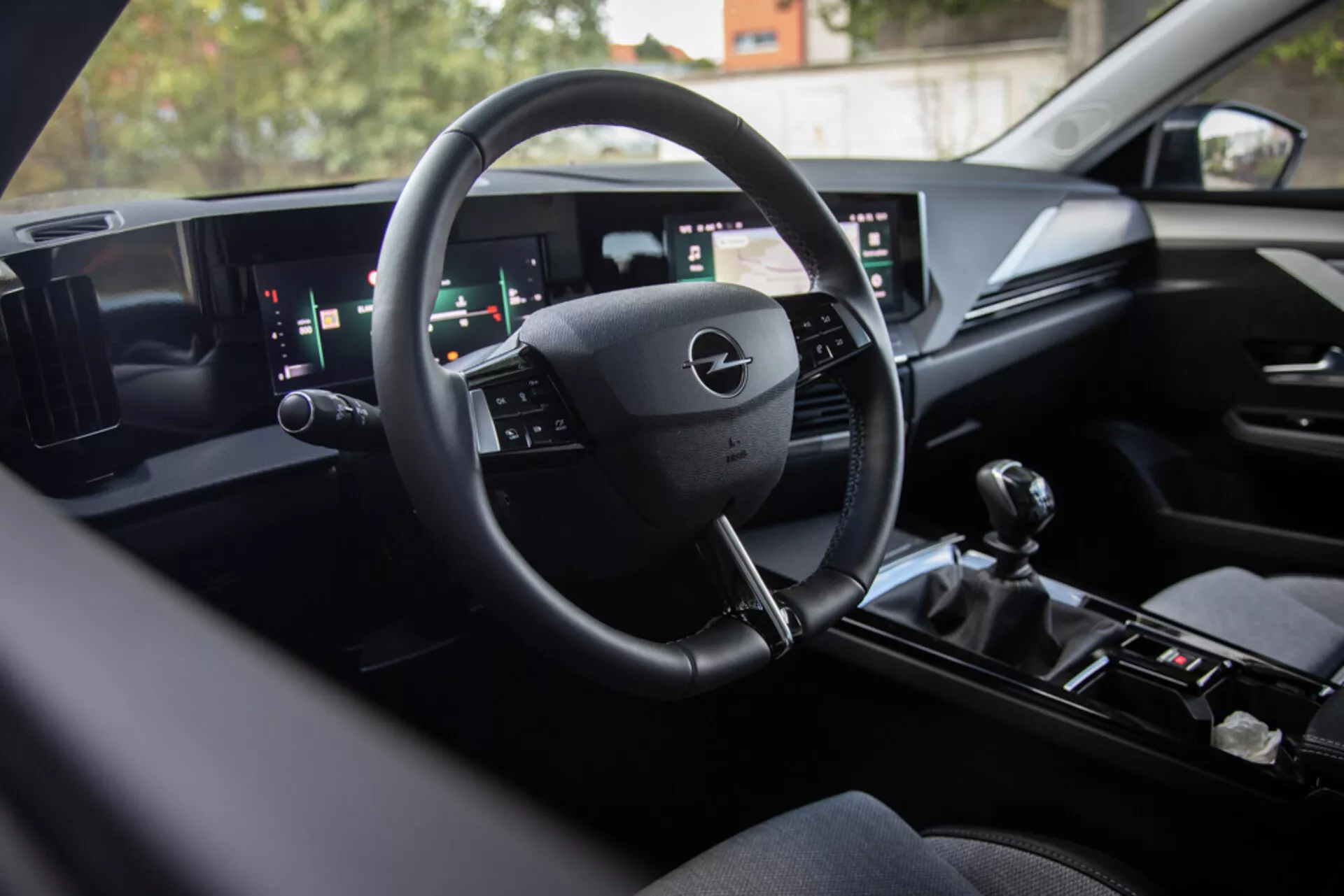 Interior del Opel Astra 2022 mostrando tecnología moderna de tablero digital, volante multifunción, sistema de infoentretenimiento de pantalla dual ancha y cambio de marchas manual para un rendimiento deportivo, visto desde el asiento trasero hacia el área del conductor con acabados premium