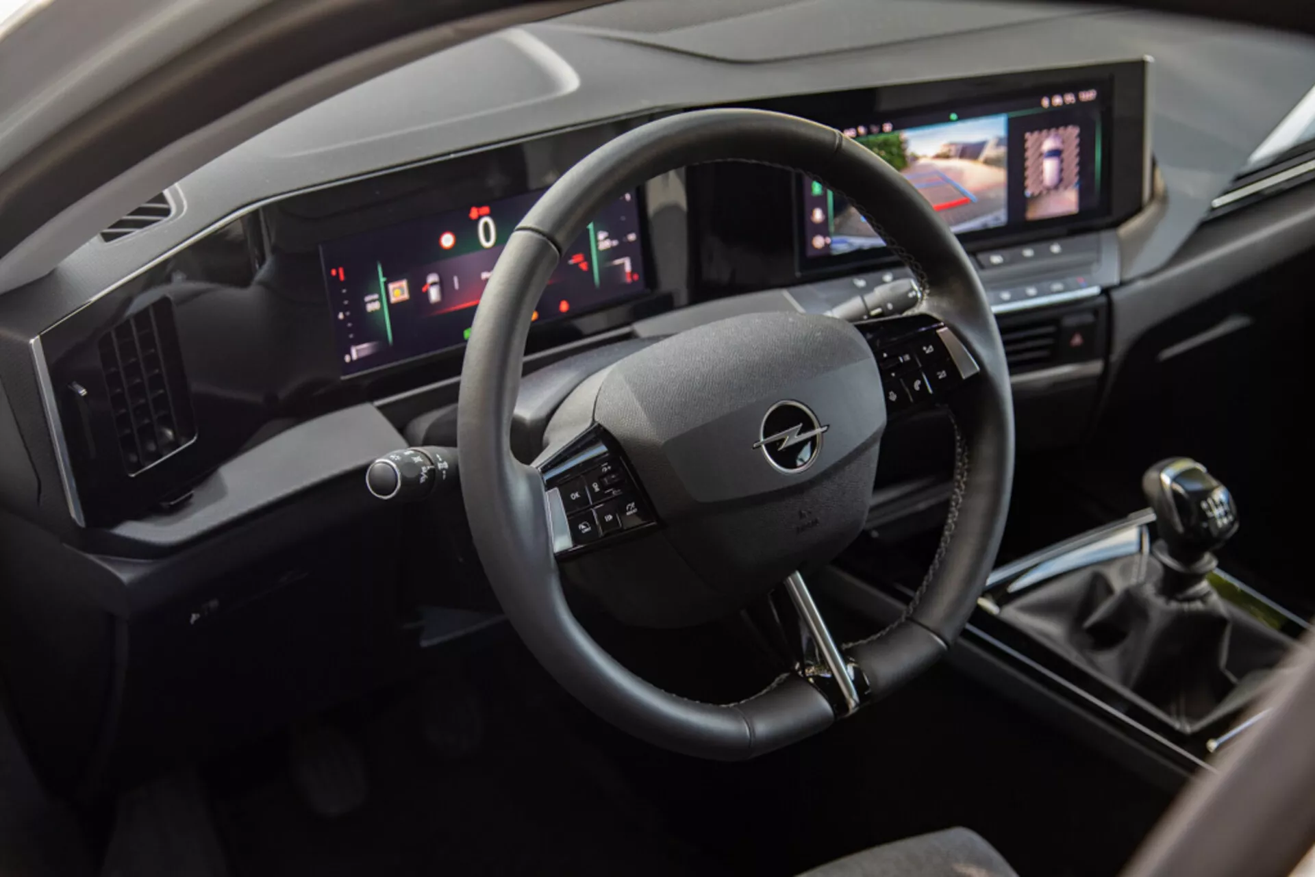 Vista interior del Opel Astra 2022 mostrando el área del conductor con un volante de tres radios, panel de instrumentos digital y consola central que incluye un sistema de información y entretenimiento táctil, cambio de marchas manual y controles modernos de climatización