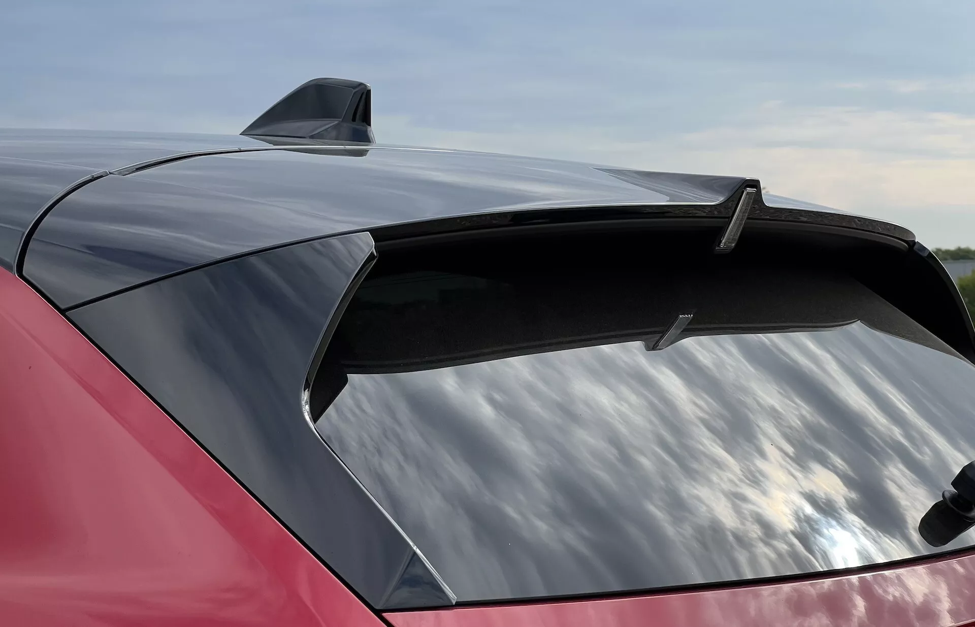 Vista de cerca de la sección trasera rojo brillante de un Opel Astra 2022 con un spoiler elegante y una antena de aleta de tiburón, destacando el amplio parabrisas trasero aerodinámico con potencial tinte de protección UV.