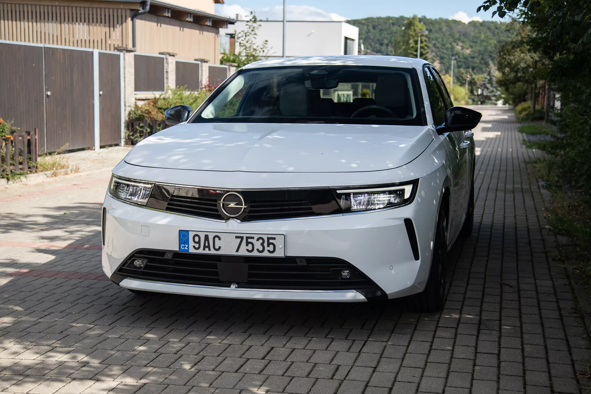 Vista frontal y lateral del Opel Astra 2022 destacando faros LED, diseño minimalista de la parrilla, ruedas de aleación parcialmente visibles y paneles de carrocería elegantes en una calle residencial europea