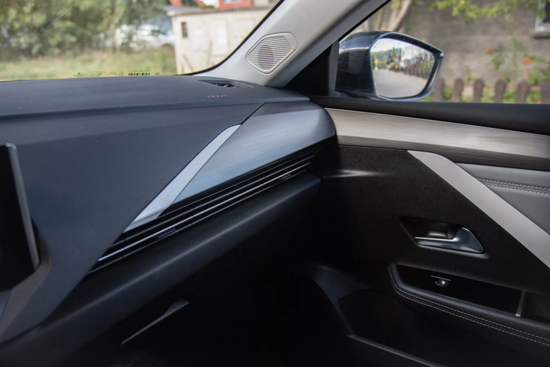 Vista interior desde la perspectiva del asiento del pasajero mostrando el diseño del tablero, acabados y panel de la puerta de un Opel Astra 2022, con líneas contorneadas elegantes y oscuras con un enfoque en la textura del material y posibles integraciones tecnológicas