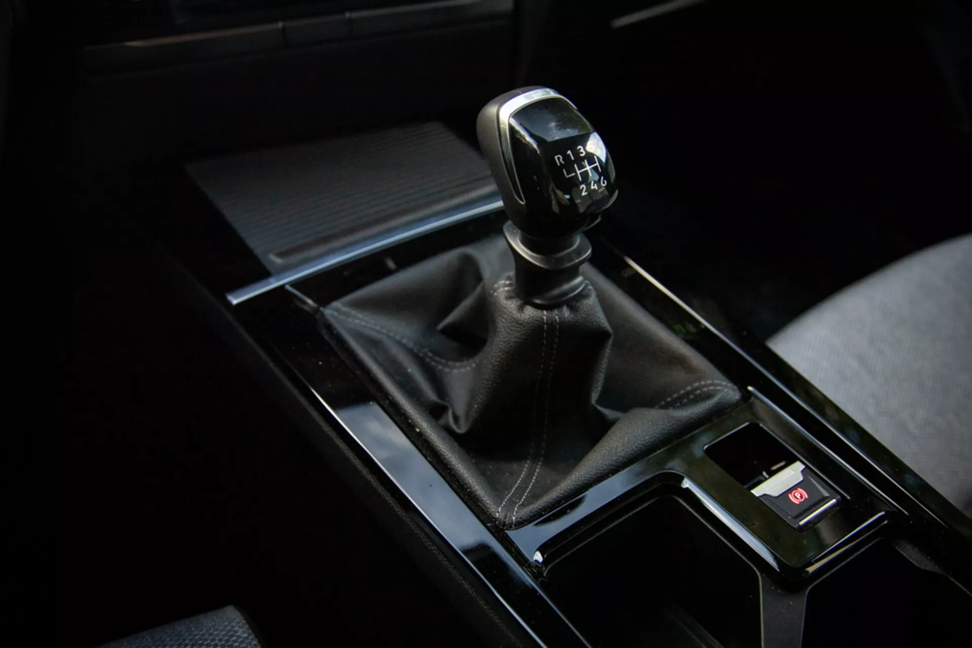 Vista de cerca de la palanca de cambios manual de un Opel Astra 2022 en la parte superior derecha del cuadro con funda de cuero, consola negra brillante y elementos interiores circundantes
