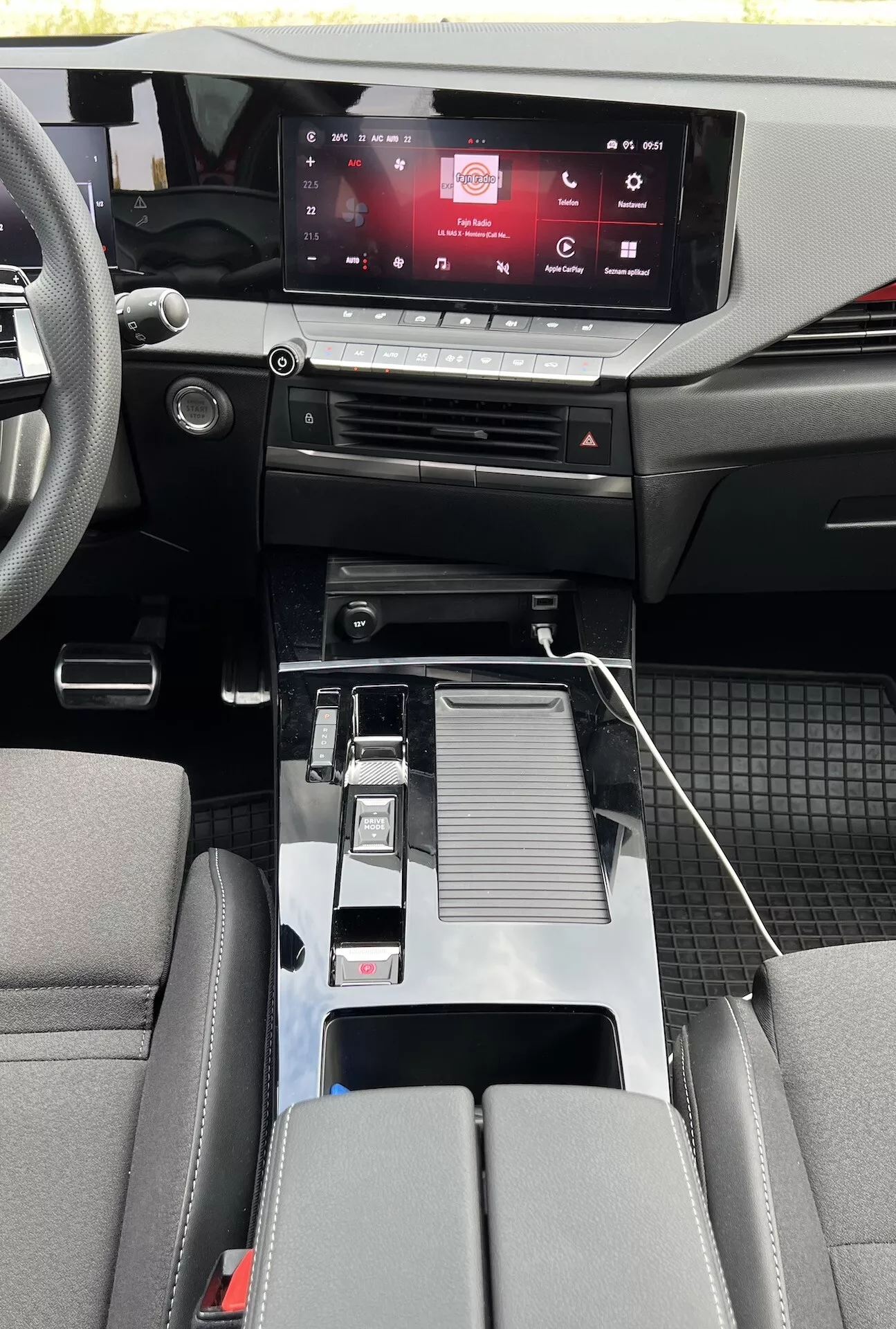 Vista interior del Opel Astra 2022 mostrando el diseño moderno de la cabina con sistema de infoentretenimiento táctil, controles climáticos sensibles al tacto, palanca de cambios metálica, conectividad USB, portavasos, reposabrazos central detallado, asientos bicolores y detalles de cabina de materiales mixtos con alfombrillas duraderas