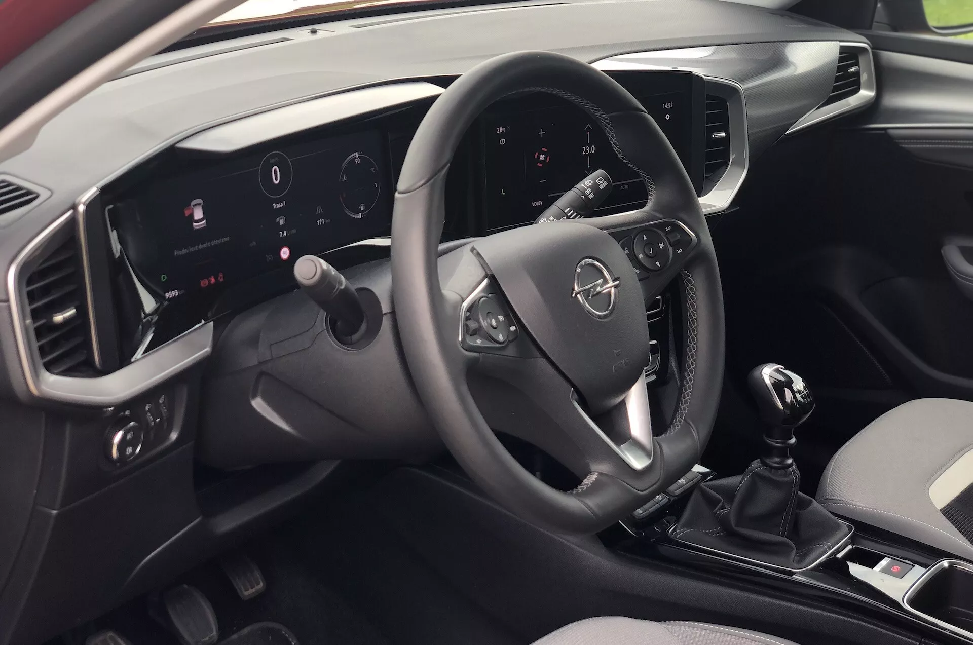 Vista interior del Opel Mokka 2021 desde la perspectiva de un pasajero en el asiento trasero del lado derecho, mostrando el moderno tablero, volante multifunción, cuadro de instrumentos digital iluminado, sistema de infoentretenimiento con pantalla táctil, cambio manual y diseño elegante en dos tonos.