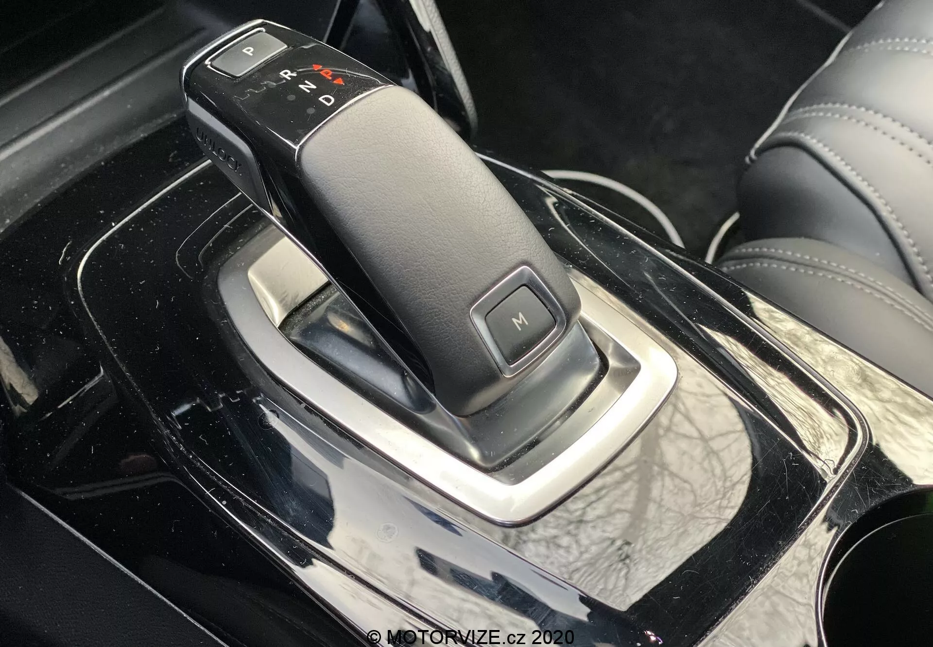 Imagen de primer plano, perspectiva lateral del interior del Peugeot 2008 2020 con elegante palanca de cambios, con transmisión automática con etiquetas 'P', 'R', 'N', 'D' y 'M' para modo manual, en una consola central negra piano brillante con detalles cromados y alrededores con apariencia de cuero, indicativo del interior de un coche premium.