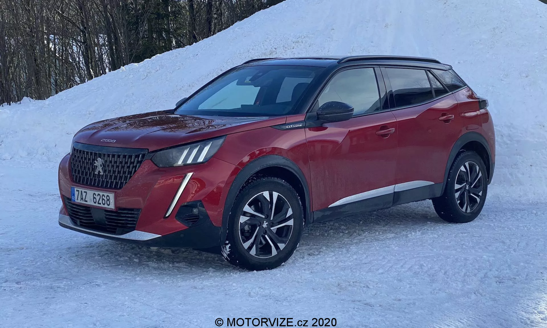 Peugeot 2008 1.2 PureTech 100 Active SUV moderno del 2020 en vista frontal de tres cuartos, resaltando la gran parrilla con patrón de diamantes, faros LED con DRL, ruedas de aleación de múltiples radios y carrocería esculpida en rojo metálico. Colocado sobre suelo nevado, insinuando capacidades de conducción en invierno como tracción en las cuatro ruedas.
