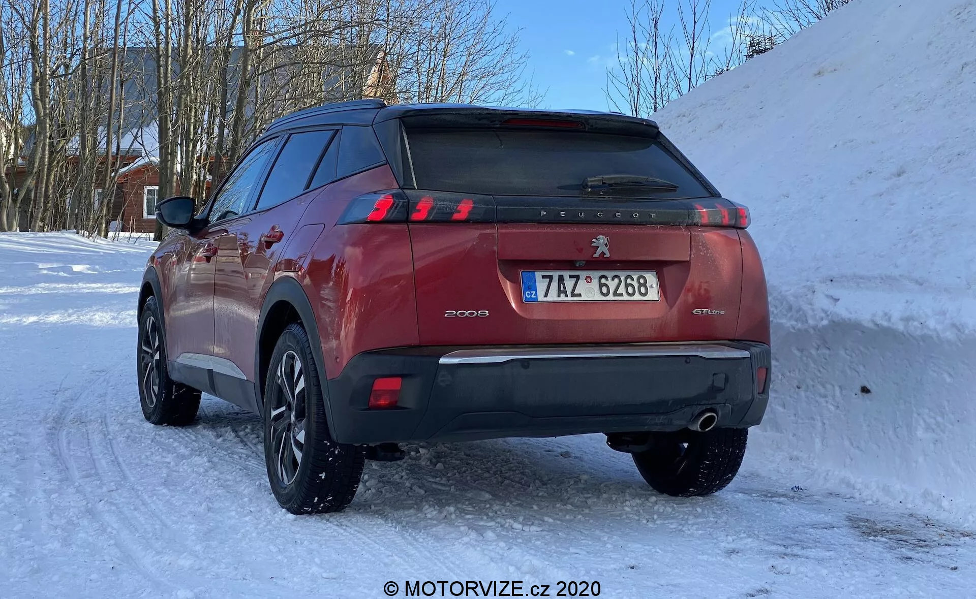 Vista de ángulo trasero de un Peugeot 3008 de color rojo estacionado en un camino nevado, mostrando la parte trasera con énfasis en el área del portón trasero, luces traseras LED de tres garras y la designación del modelo '3008'. También son visibles la insignia 'GTLINE', sistema de escape dual, rueda trasera derecha y elementos de diseño distintivos de Peugeot. El coche cuenta con llantas de aleación con neumáticos de invierno y está capturado con luz natural desde un ángulo bajo.