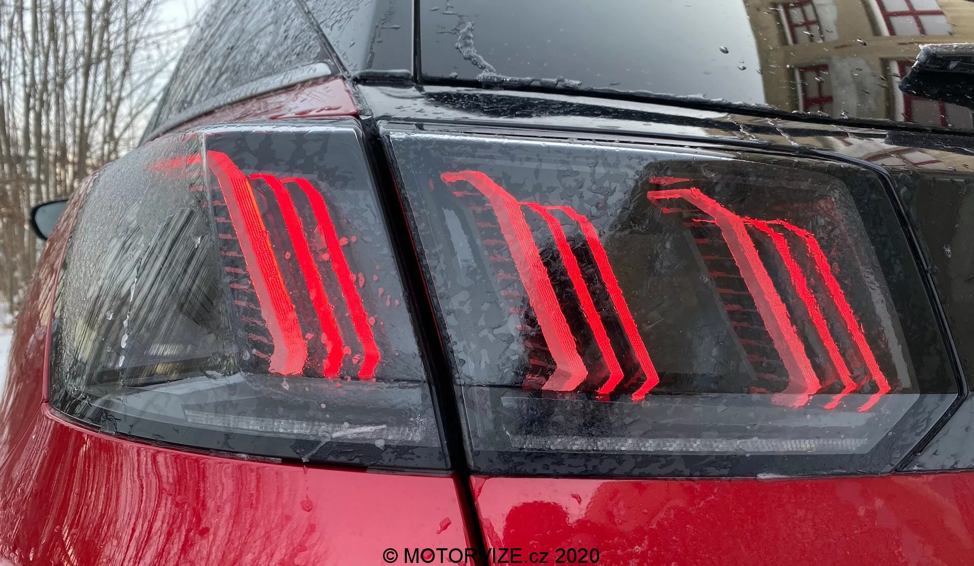 Primer plano de la parte trasera del Peugeot 3008 2021, destacando el diseño moderno de la luz trasera LED verticalmente iluminada contra su carrocería roja brillante con gotas de agua, sugiriendo un entorno al aire libre durante o después de la lluvia; la luz trasera cuenta con tecnología eficiente en energía y sirve como indicadores de luz de freno y de funcionamiento.