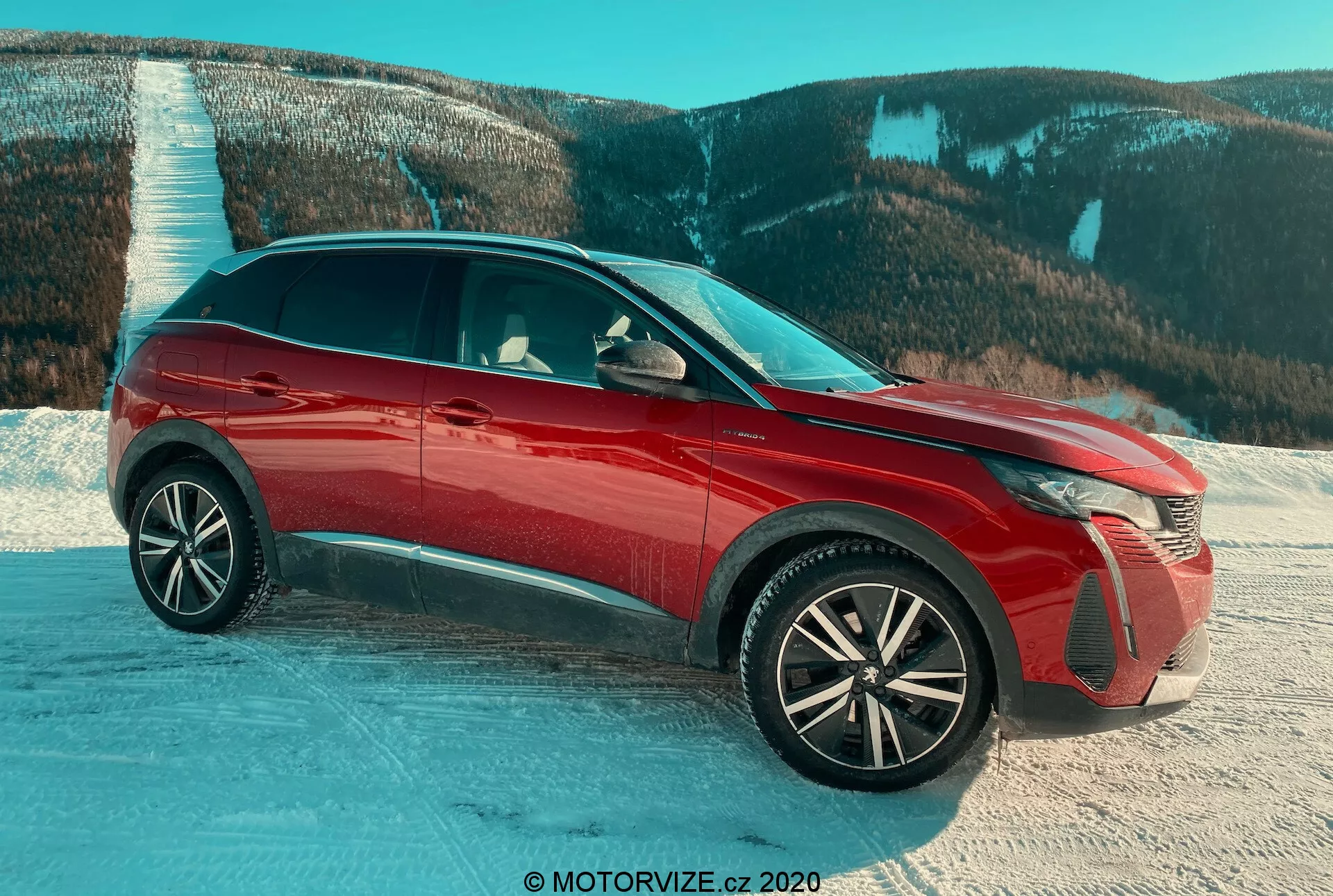 Peugeot 3008 SUV 2021 en rojo, capturado desde una vista frontal de tres cuartos sobre una superficie nevada con un fondo montañoso, destacando los faros LED avanzados, las llantas de aleación intrincadas, el acabado brillante, las rejillas de activación y los espejos laterales con intermitentes integrados, resaltando los elementos de diseño y la idoneidad para condiciones desafiantes.