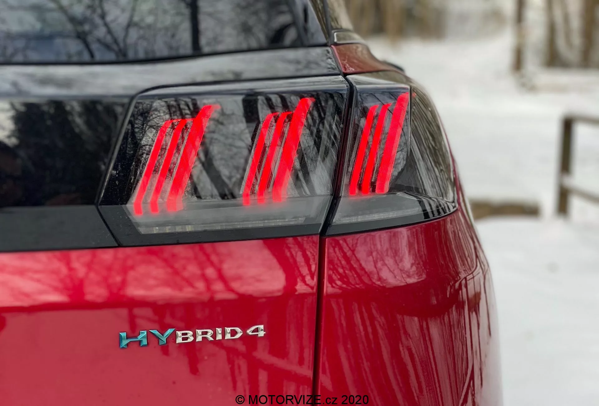 Peugeot 3008 Hybrid4 2021 - Vista trasera izquierda en ángulo mostrando la pintura roja vibrante, ensamblaje de luces traseras LED rojas modernas con segmentos verticales distintos, tapa del maletero y la insignia híbrida en la esquina trasera izquierda que indica un sistema de propulsión híbrido con posible capacidad de tracción en las cuatro ruedas.