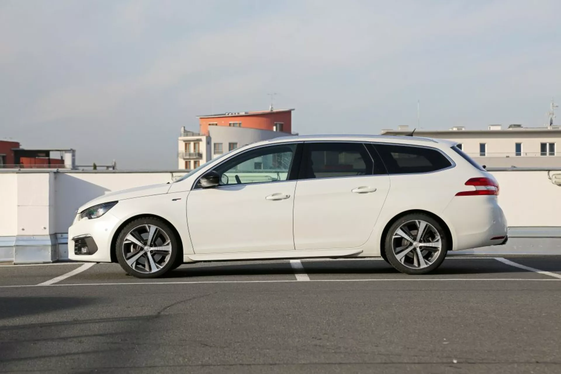 Station wagon blanco Peugeot 3008 de 2016 estacionado sobre asfalto, vista lateral de perfil destacando faros elegantes, ruedas de aleación de múltiples radios, espejos laterales del color de la carrocería y cinco puertas