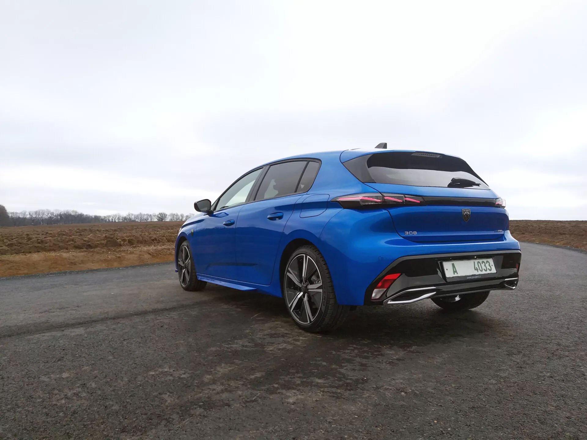 Hatchback Peugeot 308 2022 en azul vibrante, vista trasera de tres cuartos destacando luces traseras LED, spoiler integrado y ruedas de aleación de múltiples radios contra un cielo nublado.