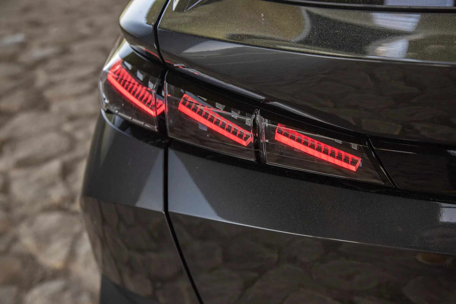 Vista cercana de las luces traseras negras brillantes del Peugeot 408 2023, con elementos LED modernos y elegantes acentos de diseño capturados desde un ángulo elevado