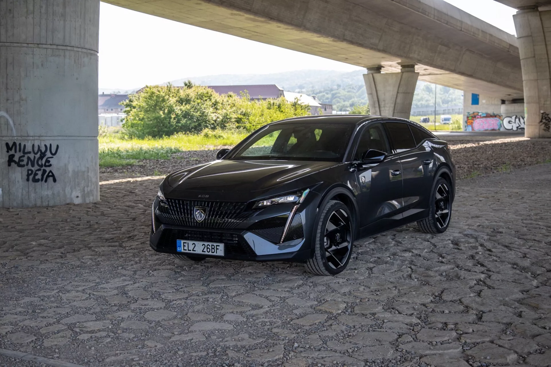 Peugeot 408 2023 capturado desde un ángulo de tres cuartos que destaca sus elegantes faros LED, parrilla estampada y parachoques frontal deportivo aerodinámico bajo luz natural del día en un área pavimentada bajo un paso elevado