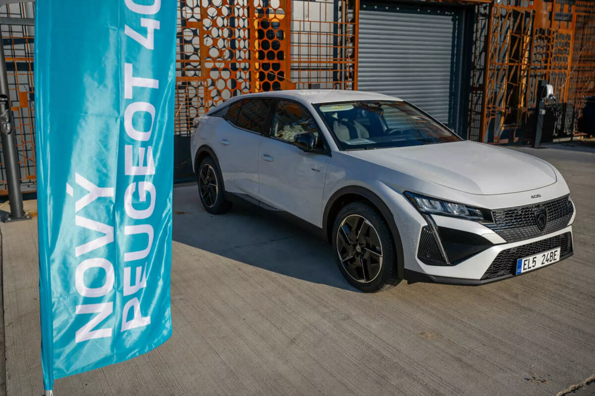 Peugeot 408 blanco del 2023 estacionado al aire libre con arquitectura industrial de fondo, mostrando las características de diseño y tecnología del vehículo bajo la luz natural del día